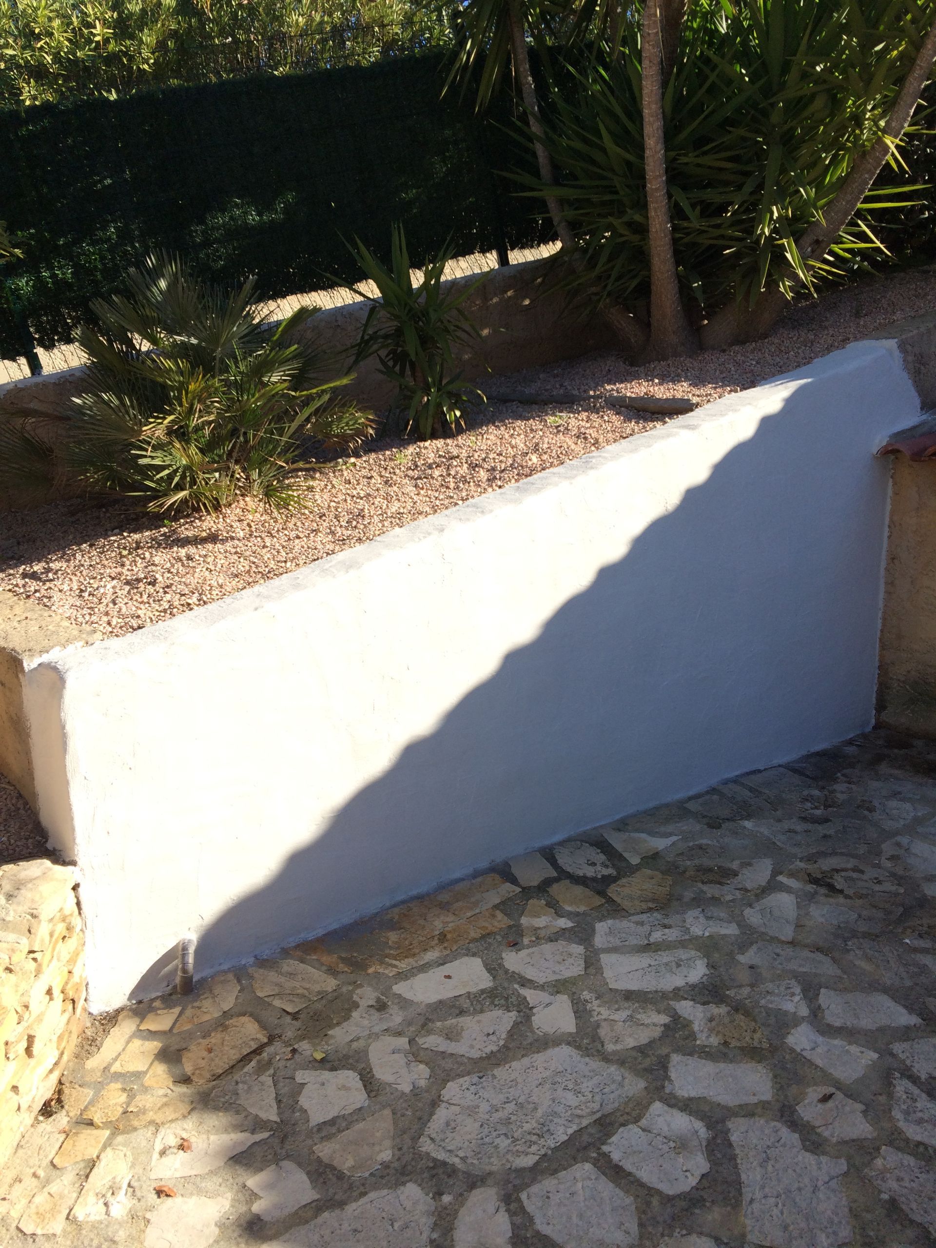 Mur extérieur récemment plâtré en blanc. Le sol est en pierres naturelles de différentes tailles et formes.
