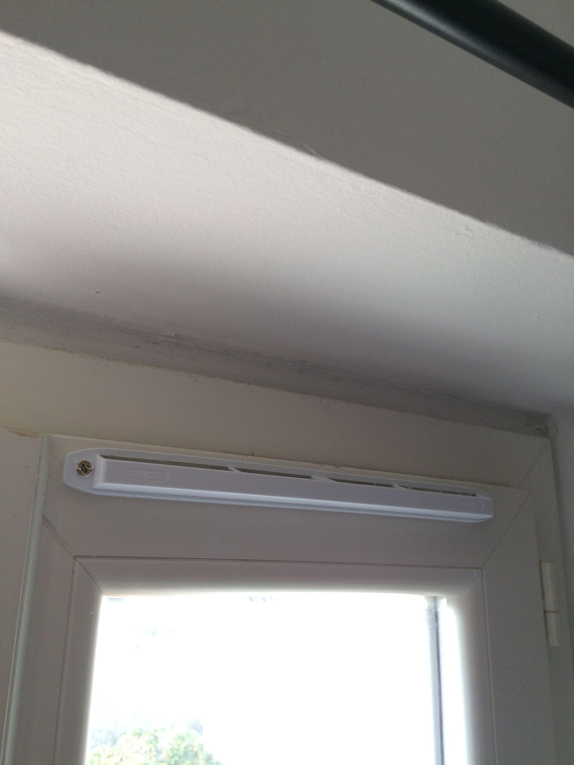 Ventilateur mural blanc installé au-dessus d'une fenêtre. Le plafond montre des signes de moisissure.