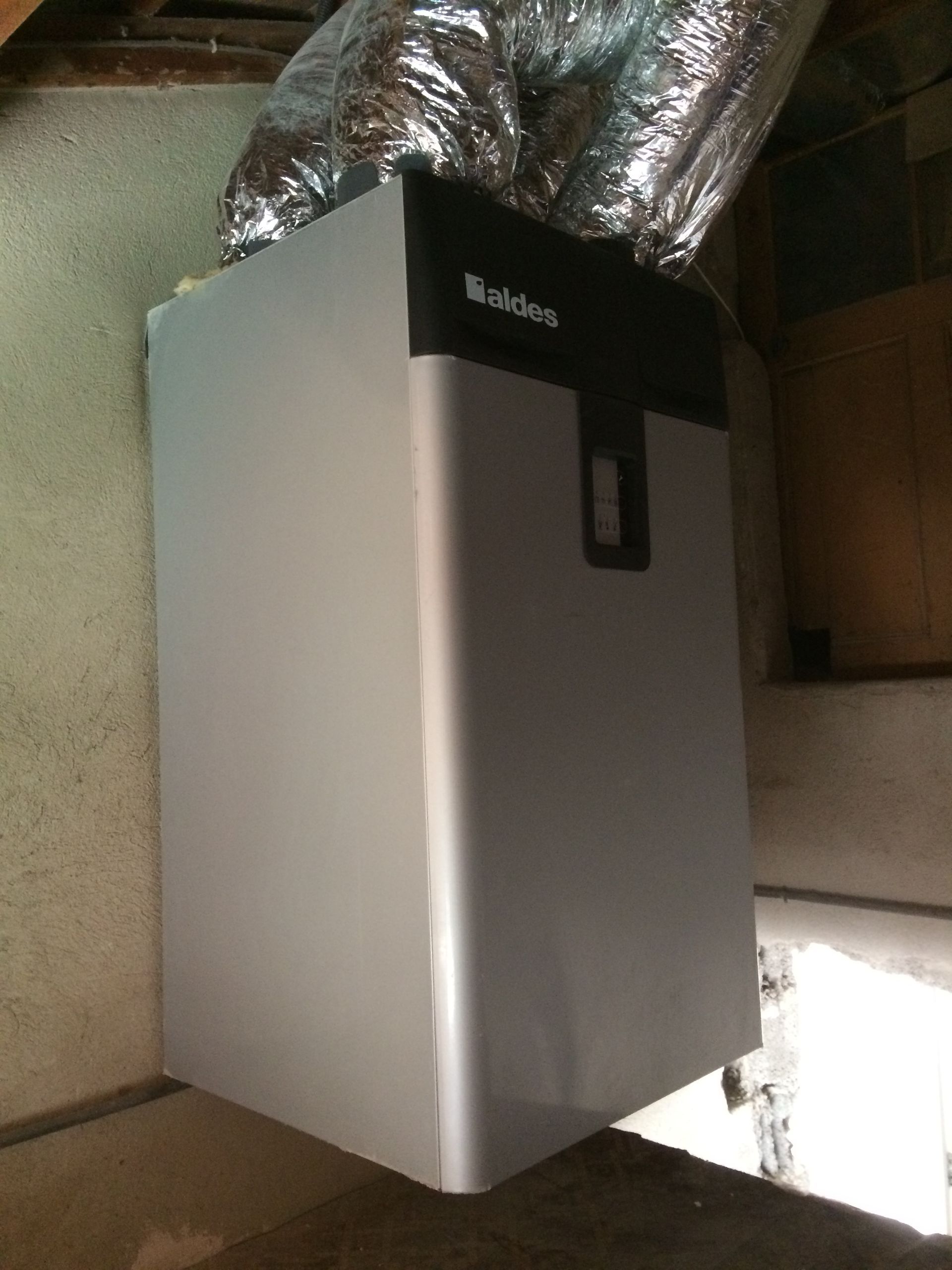 Une chaudière murale de marque Aldes, avec des conduits d'aération en aluminium au-dessus.