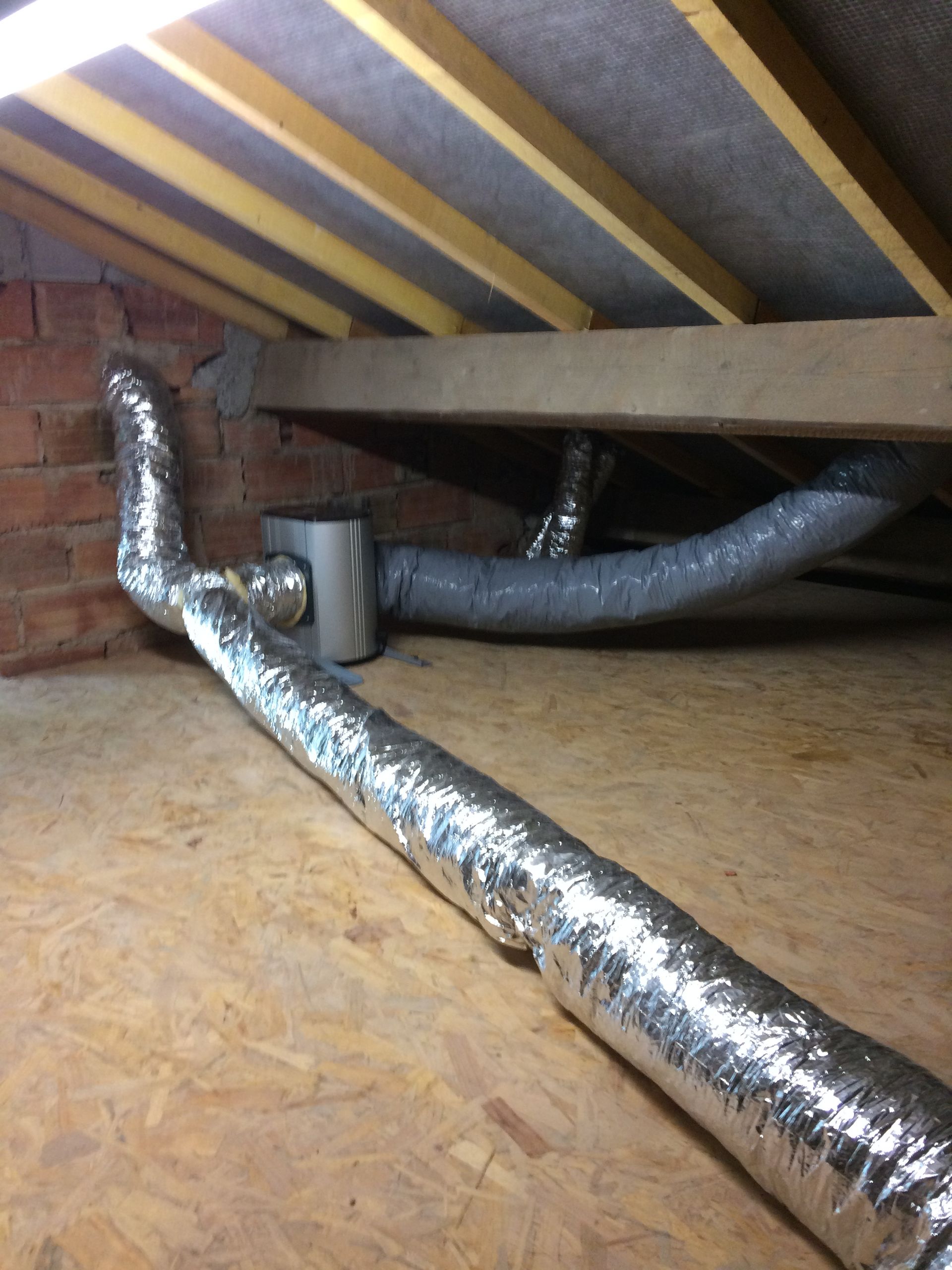 Des conduits d'aération en aluminium installés dans un grenier, avec des tuyaux isolés.