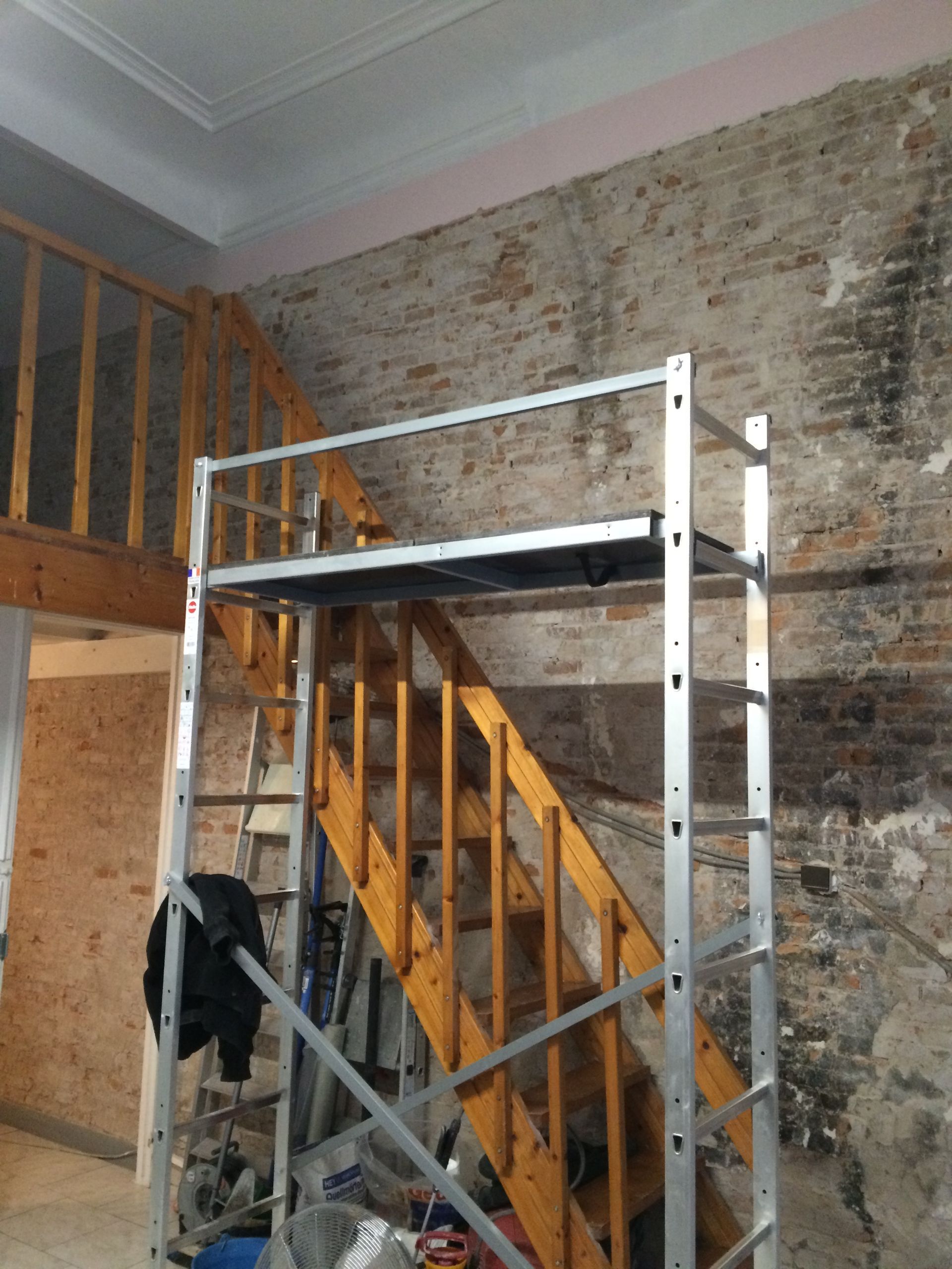 Une structure métallique temporaire installée dans une pièce en rénovation, avec des murs en briques apparentes.
