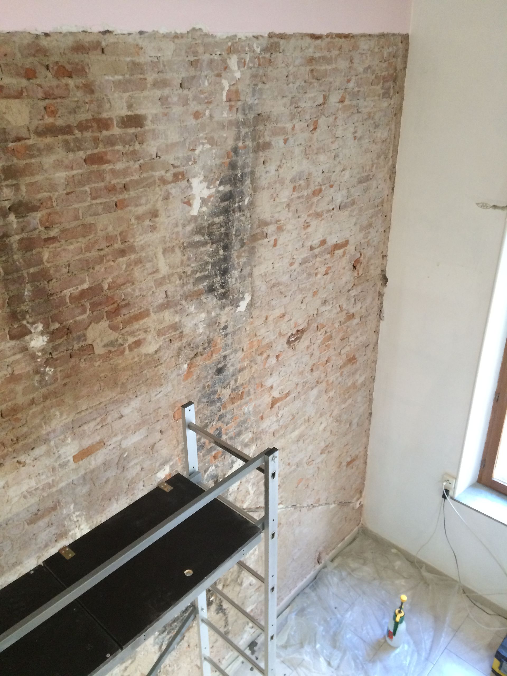 Un mur en briques apparentes avec des traces de plâtre et de mortier, et une structure métallique temporaire devant.