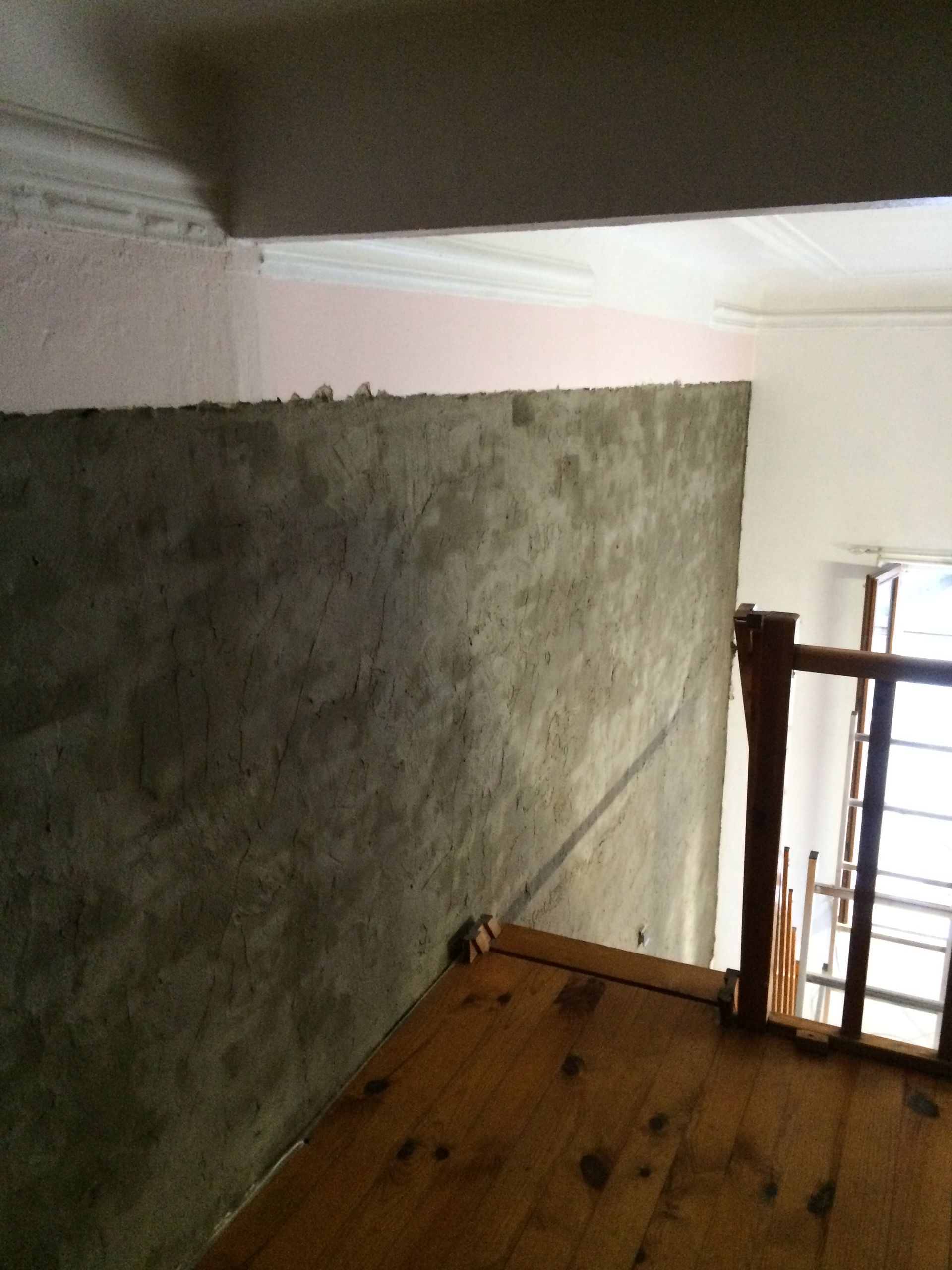 Un mur partiellement recouvert de mortier, avec une partie du mur en briques encore visible.