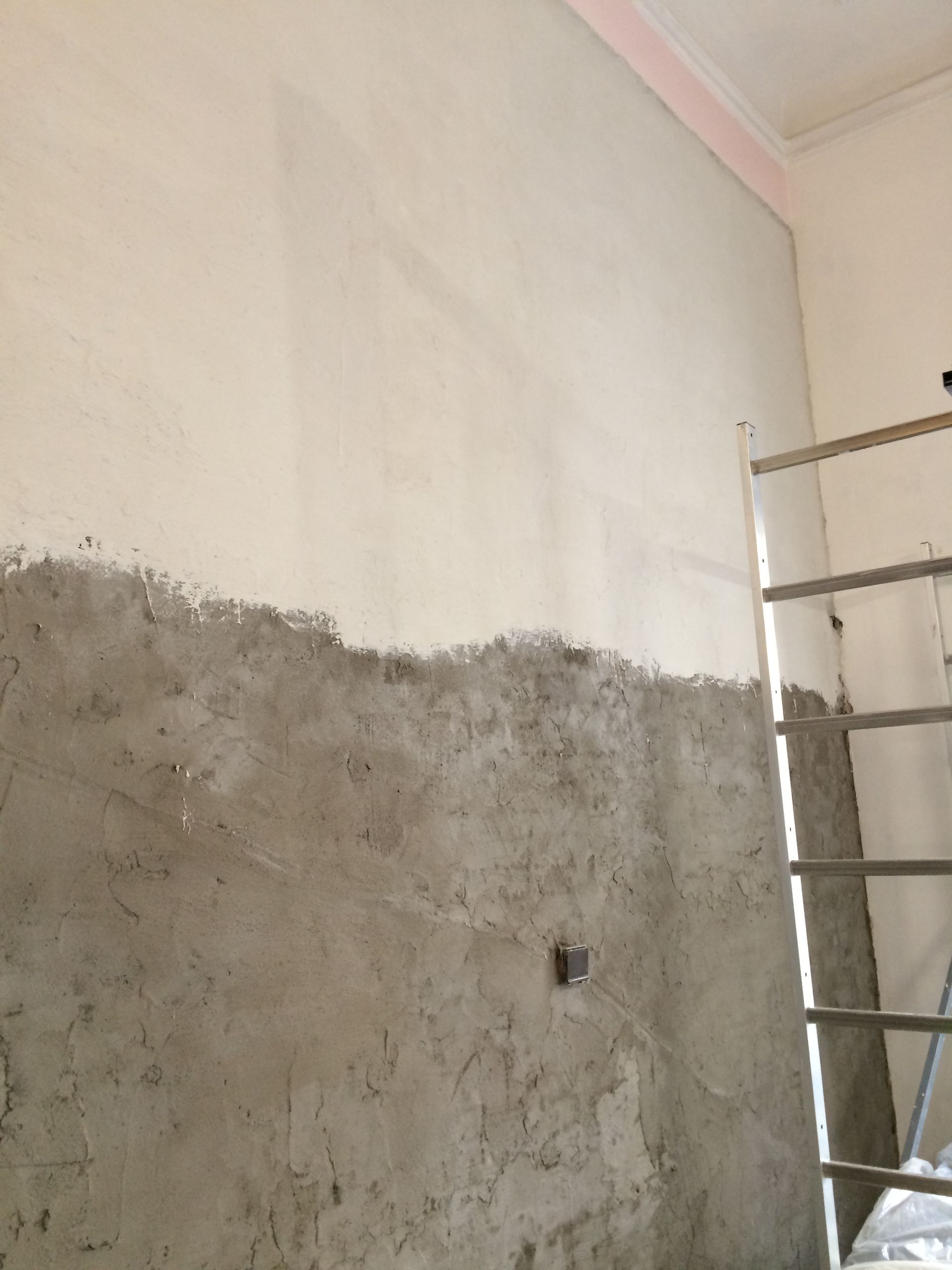 Un mur en cours de rénovation, avec la partie inférieure recouverte de mortier et la partie supérieure encore en plâtre.