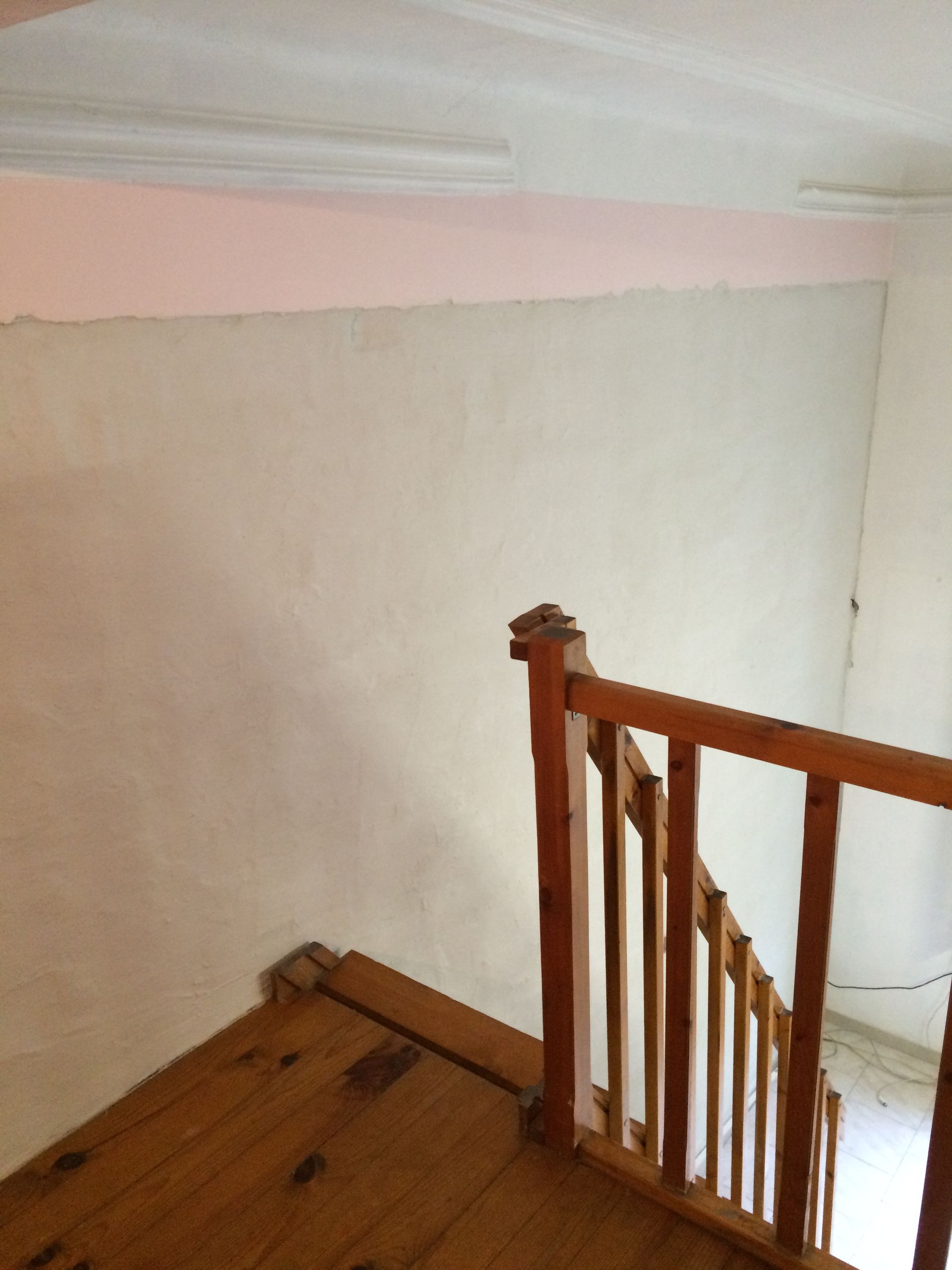 Mur blanc avec moulure et plancher en bois, escalier en bois partiellement visible.