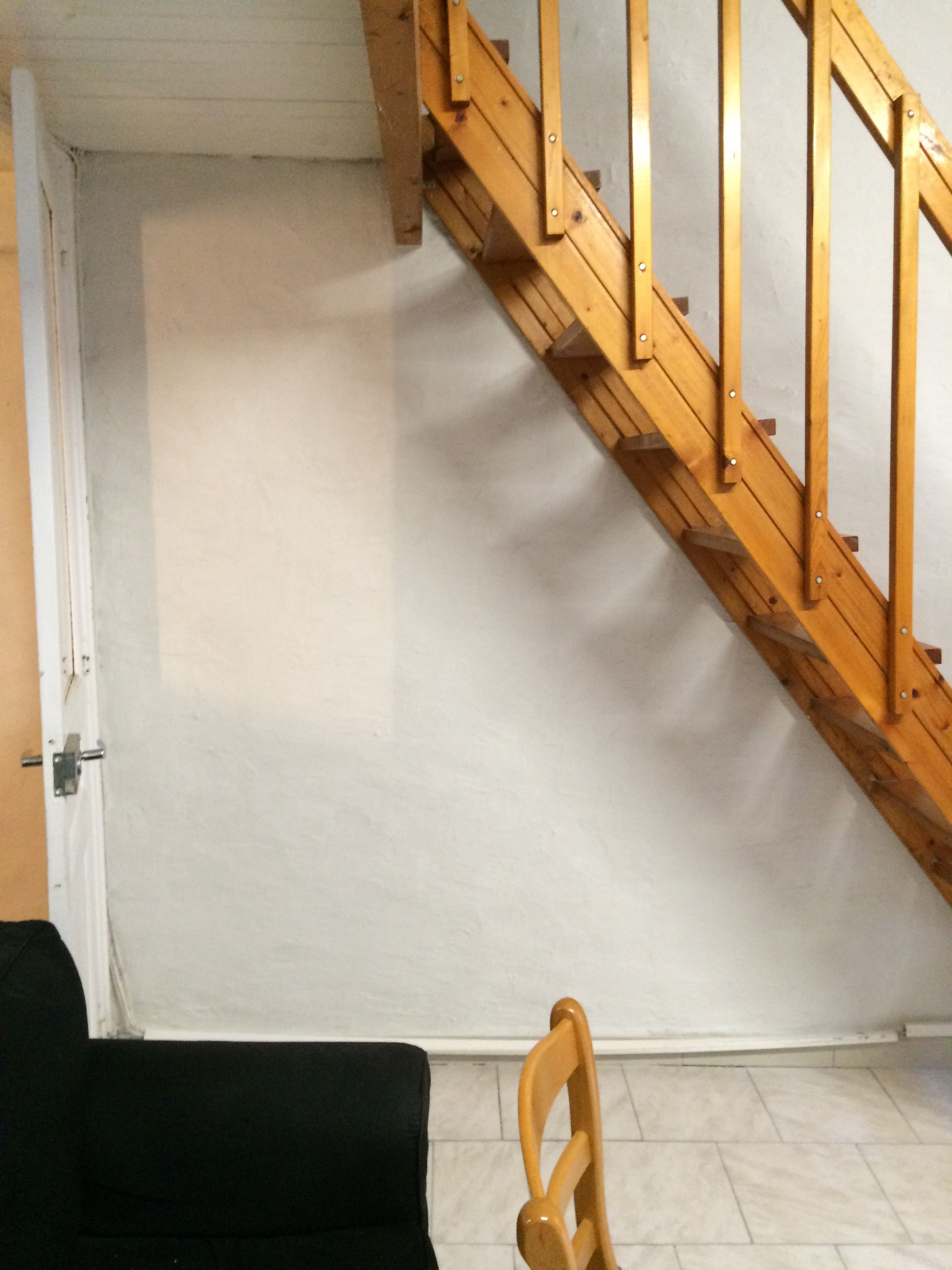 Escalier en bois avec rampe, mur blanc avec traces de peinture rose.