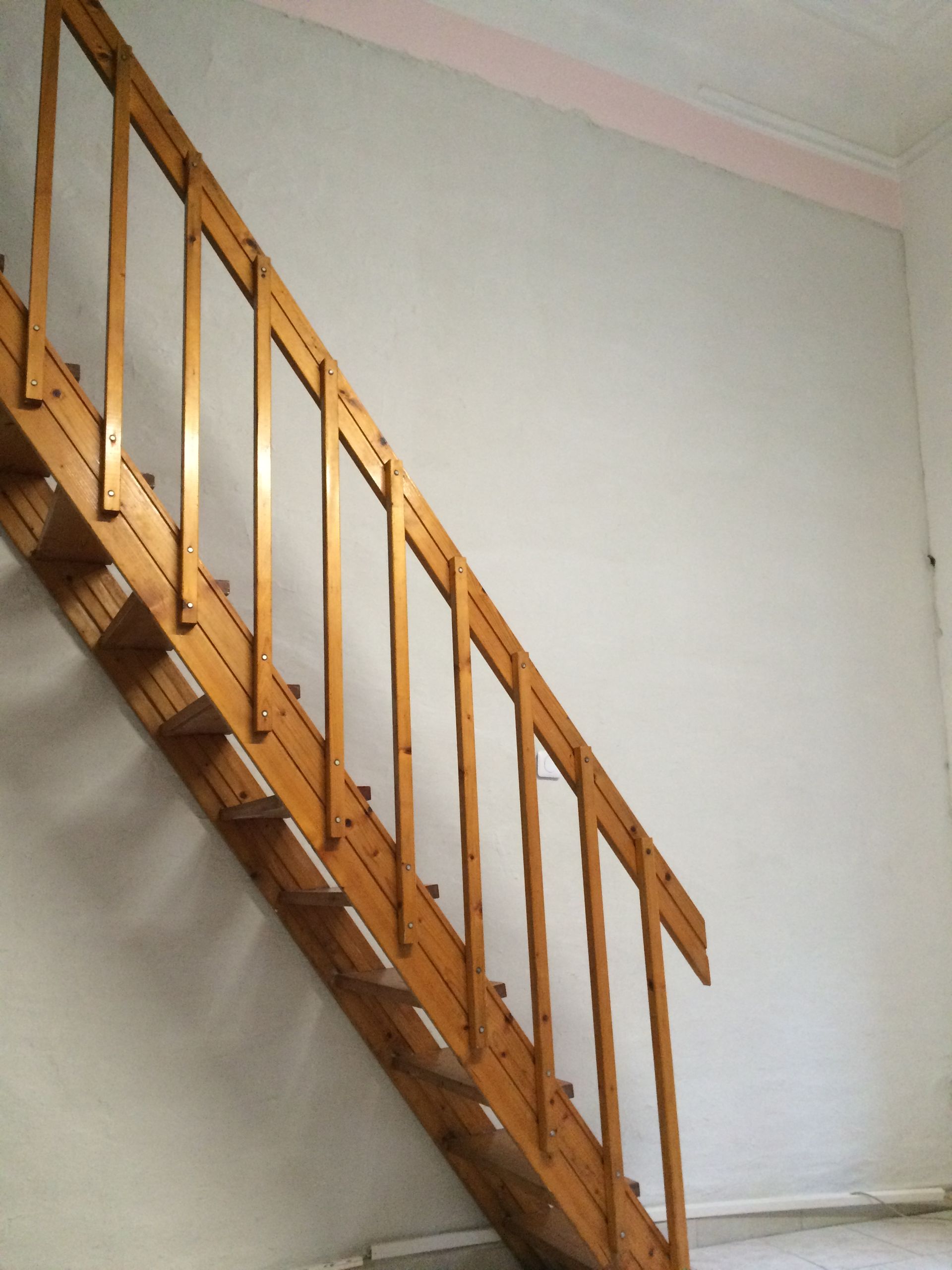 Mur blanc usé avec traces de peinture rose et escalier en bois.