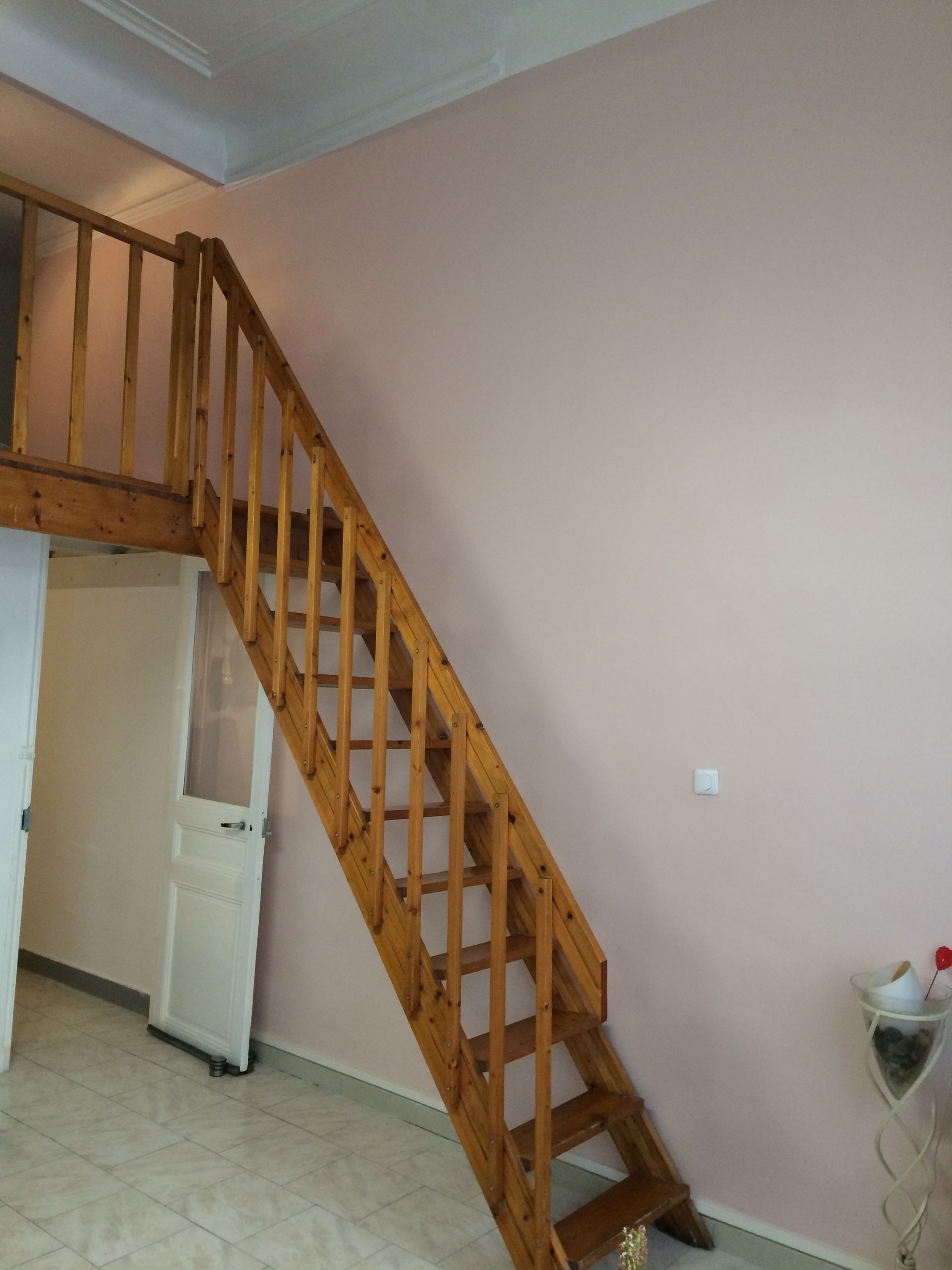 Mur rose avec escalier en bois et petite armoire blanche en dessous