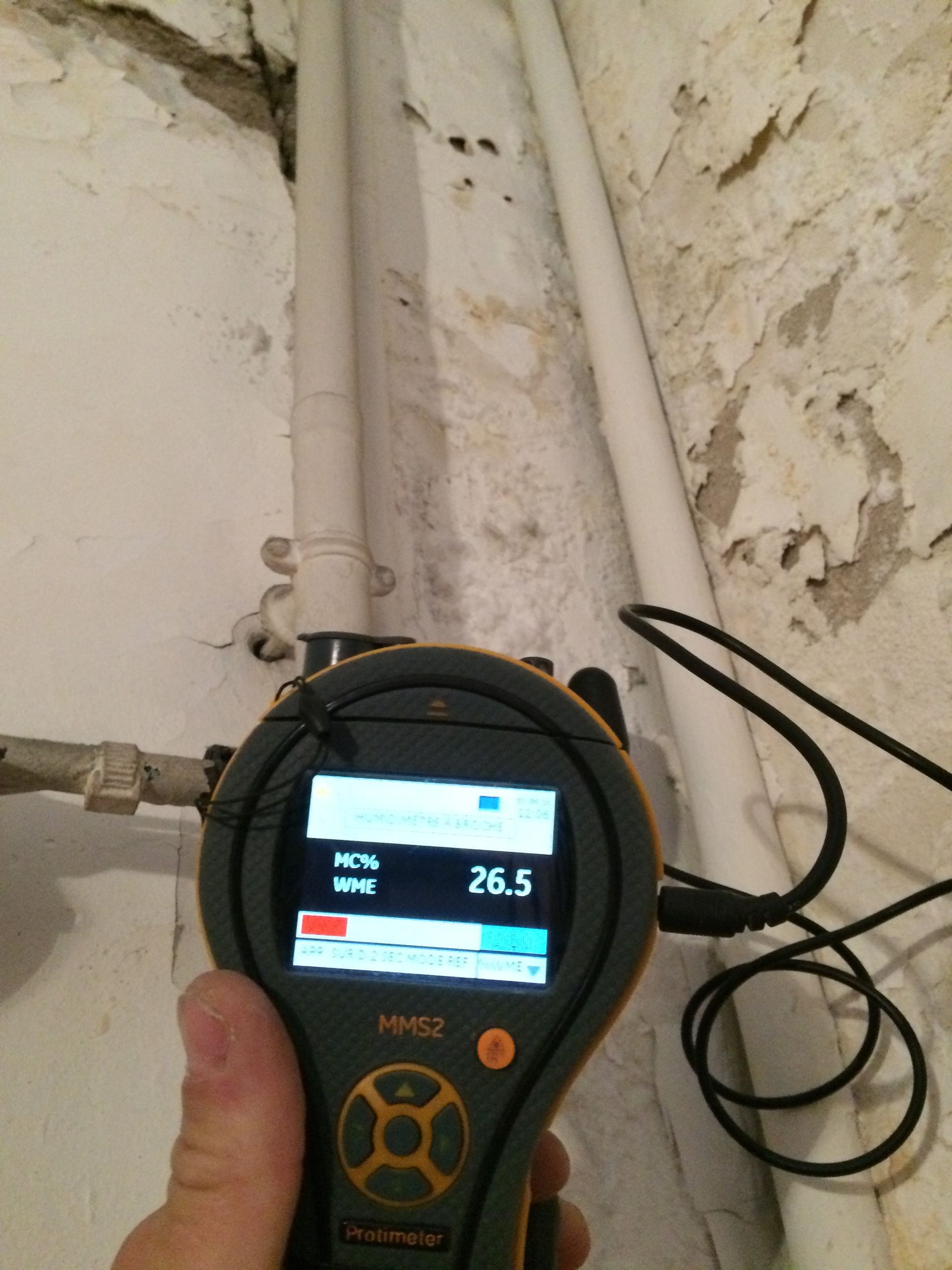 Appareil de mesure devant un mur avec tuyaux, affichant MC96 WME 26.5.
