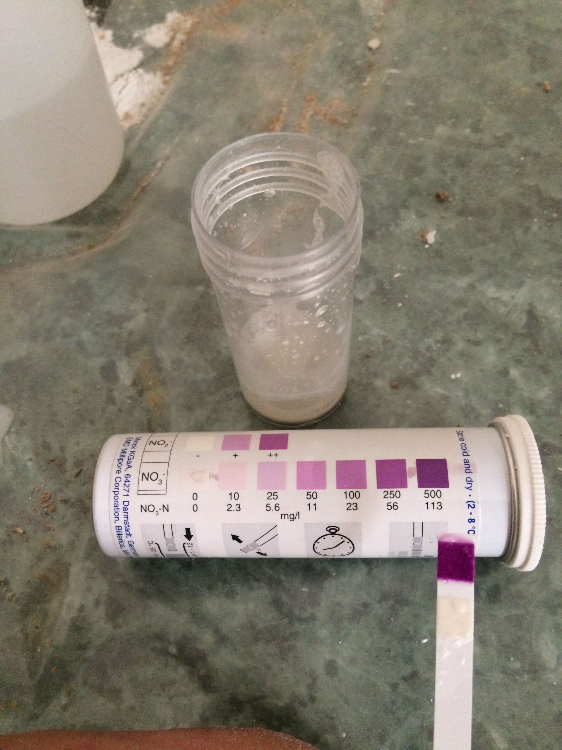 Test de nitrate montrant une bandelette de test avec un résultat positif, comparée à une échelle de couleurs sur un tube.