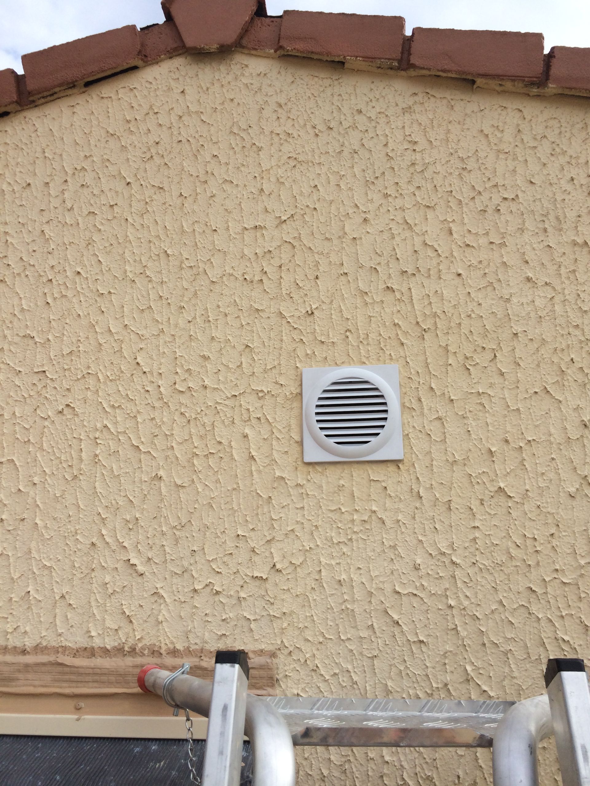 Ventilation installée sur un mur extérieur en stuc, avec une finition rugueuse.