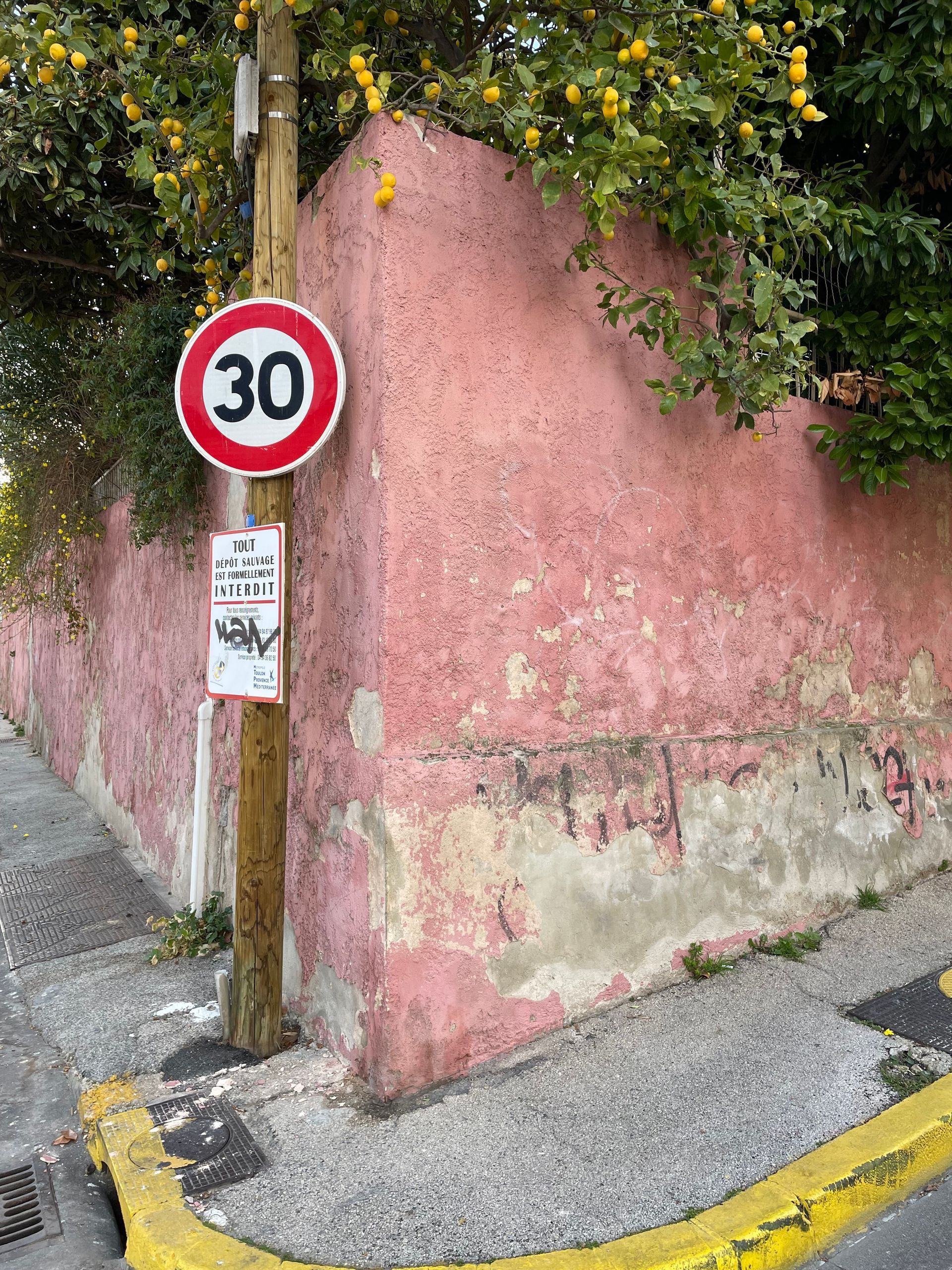 Mur extérieur rose avec des signes de dégradation, situé près d'un panneau de signalisation.
