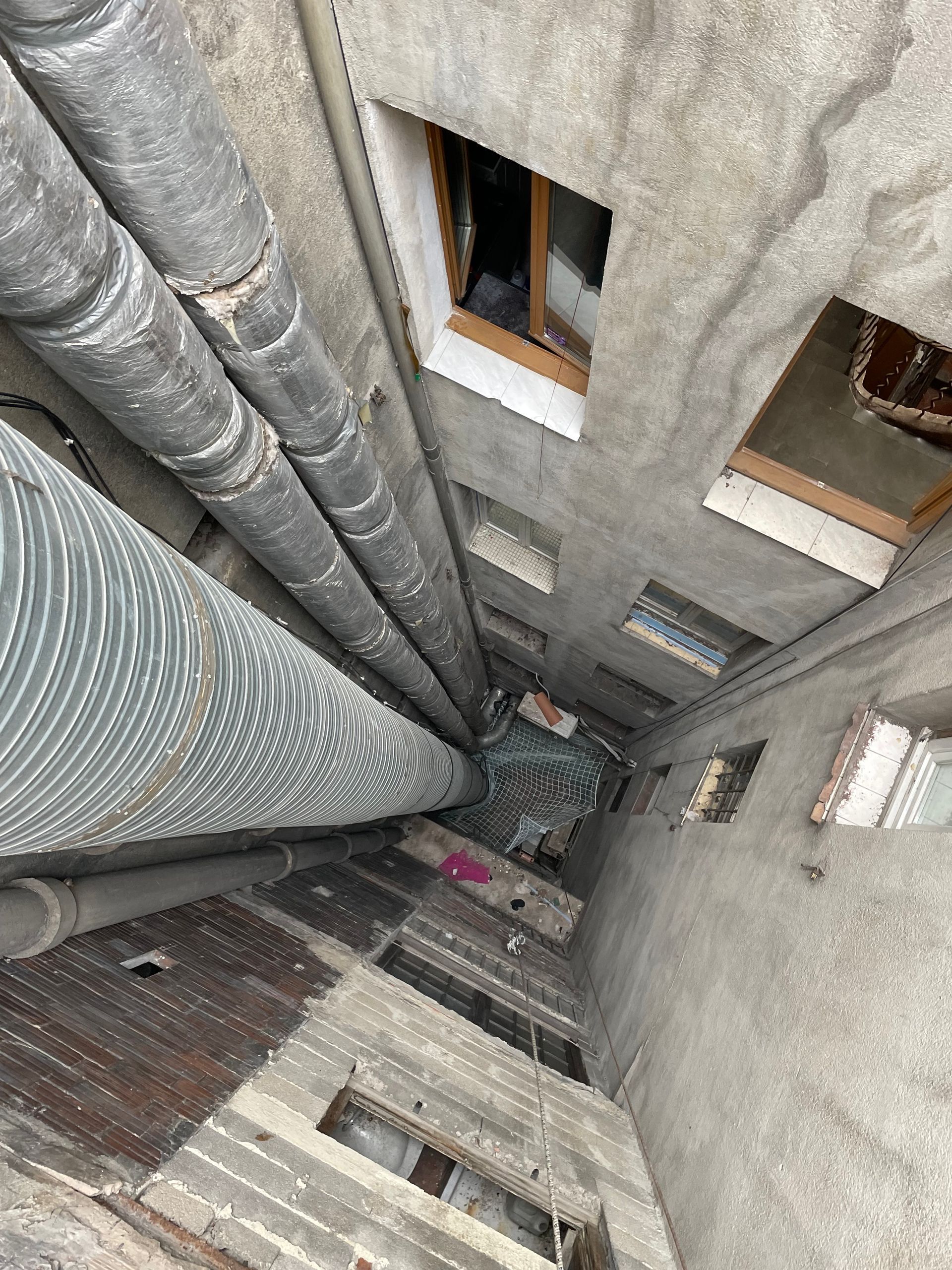 Vue d'un espace intérieur avec des tuyaux et des conduits. Les murs sont gris et il y a des ouvertures sans portes ni fenêtres.
