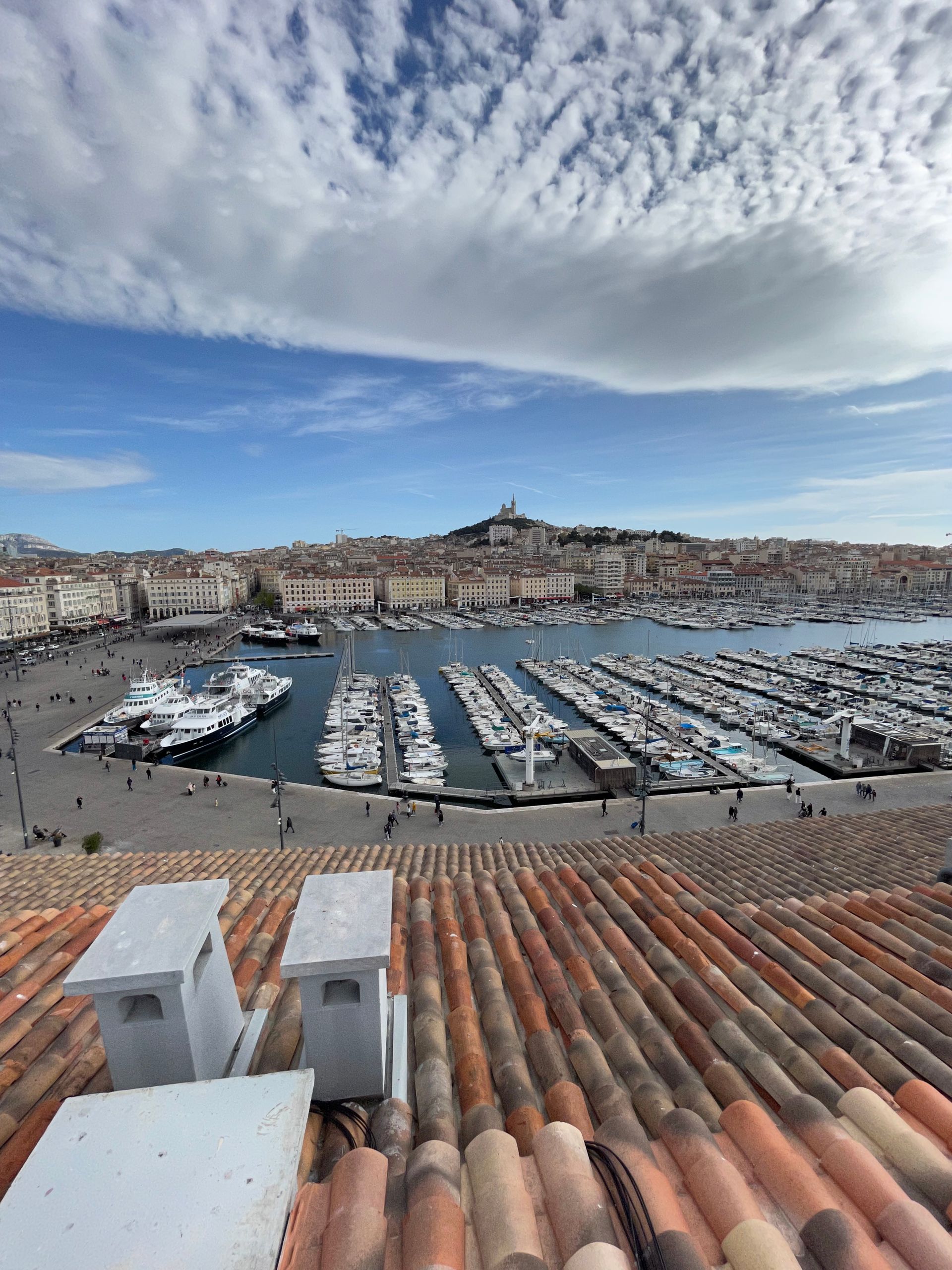 Vue d'un port de plaisance avec de nombreux bateaux amarrés. Le ciel est bleu avec quelques nuages.