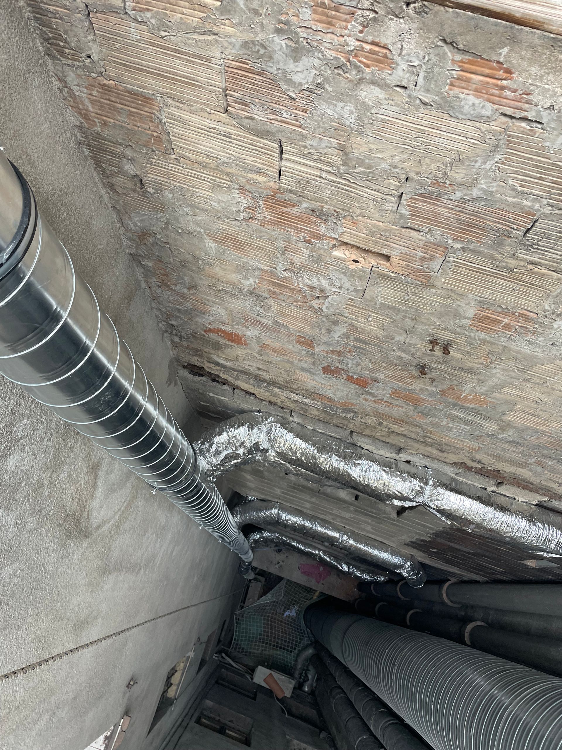 Vue rapprochée de tuyaux métalliques avec des raccords. Les tuyaux sont fixés au mur et au sol.