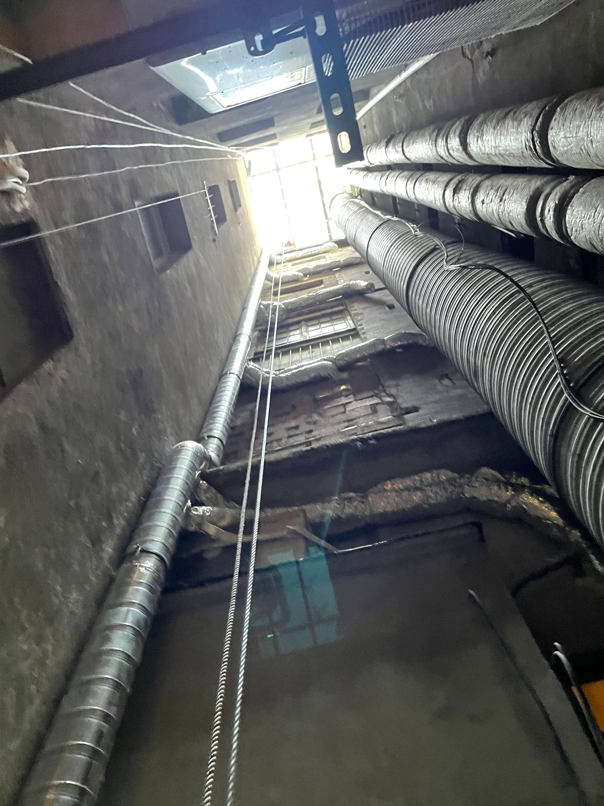 Vue de l'intérieur d'un faux plafond montrant des conduits d'aération et des câbles électriques. Les conduits sont en métal et bien organisés.