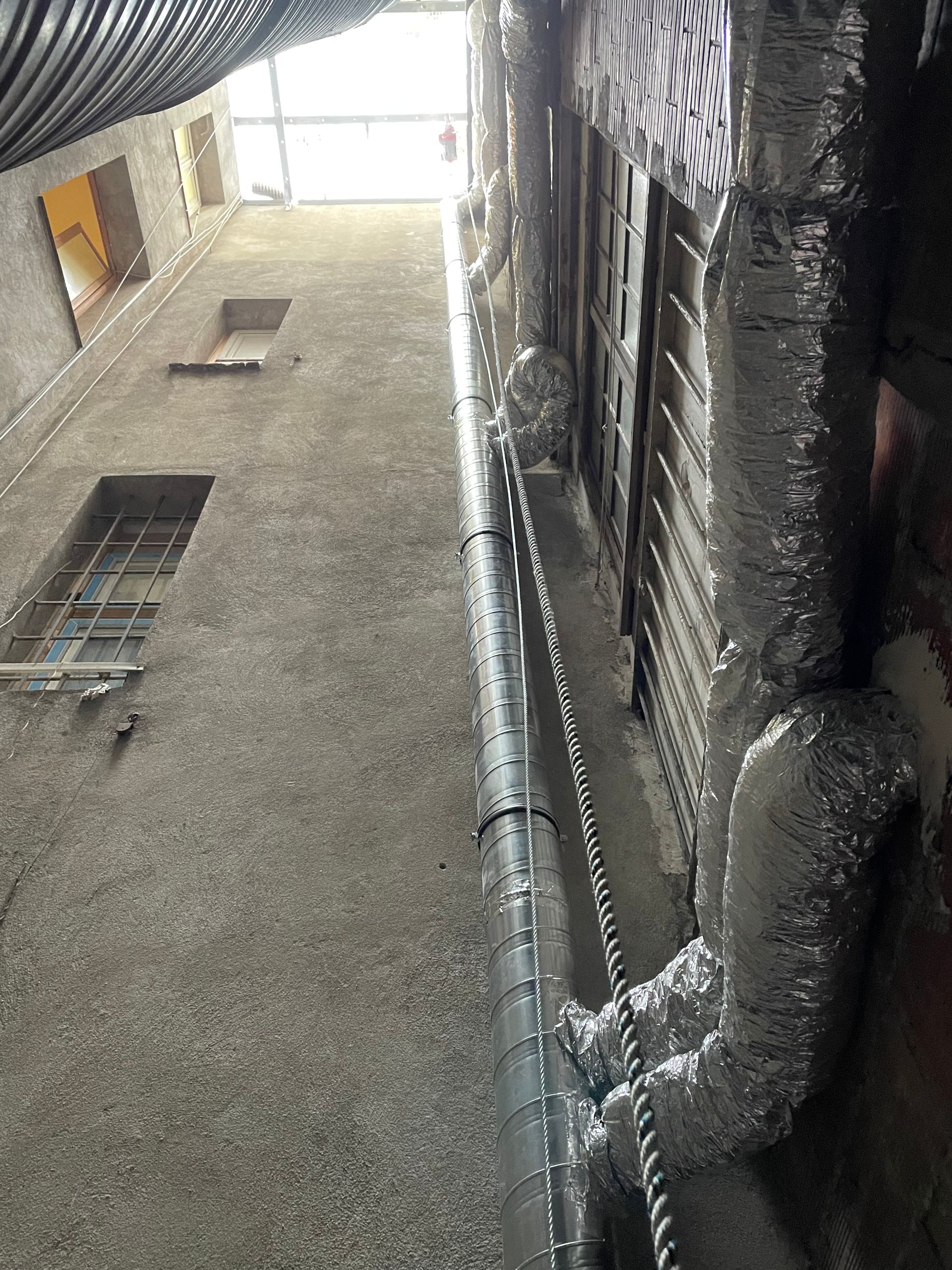 Vue d'un plafond avec des conduits d'aération et des gaines isolées. Les murs sont recouverts d'une couche de matériau isolant.