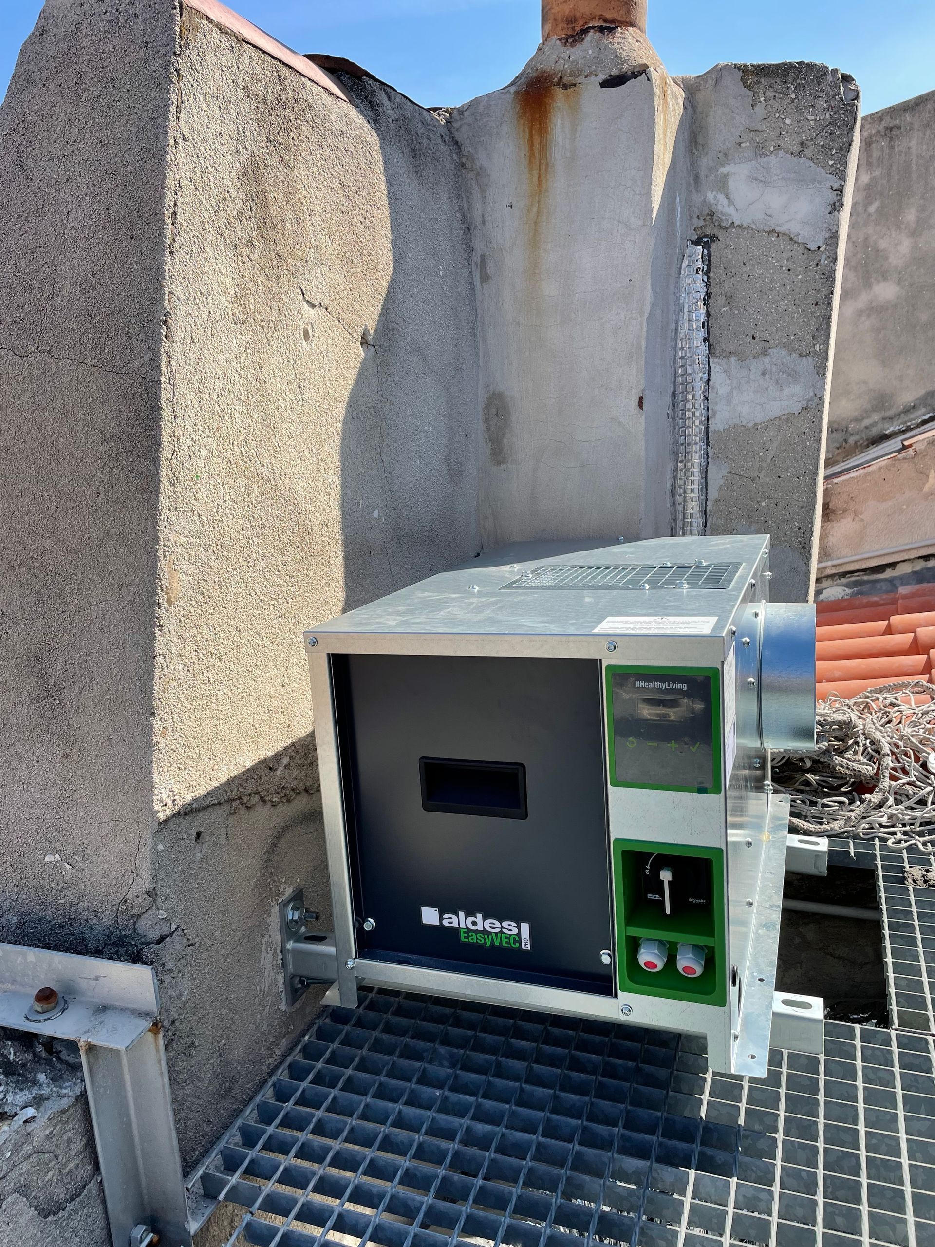Un système de ventilation mécanique contrôlée (VMC) installé sur un toit. L'appareil est fixé sur une surface en béton et est relié à des conduits d'aération.