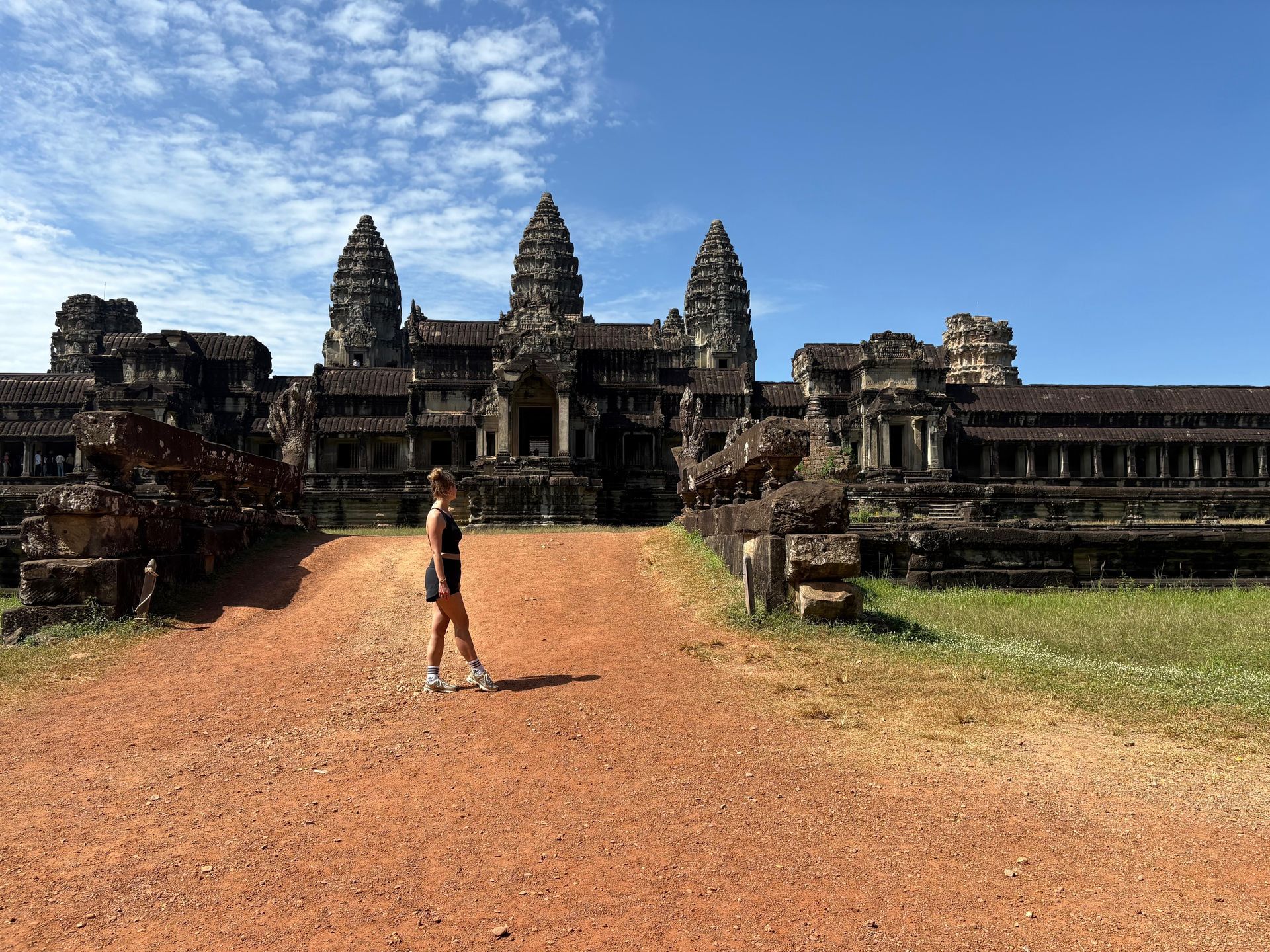 Eine Person steht vor den Steintürmen von Angkor Wat unter blauem Himmel