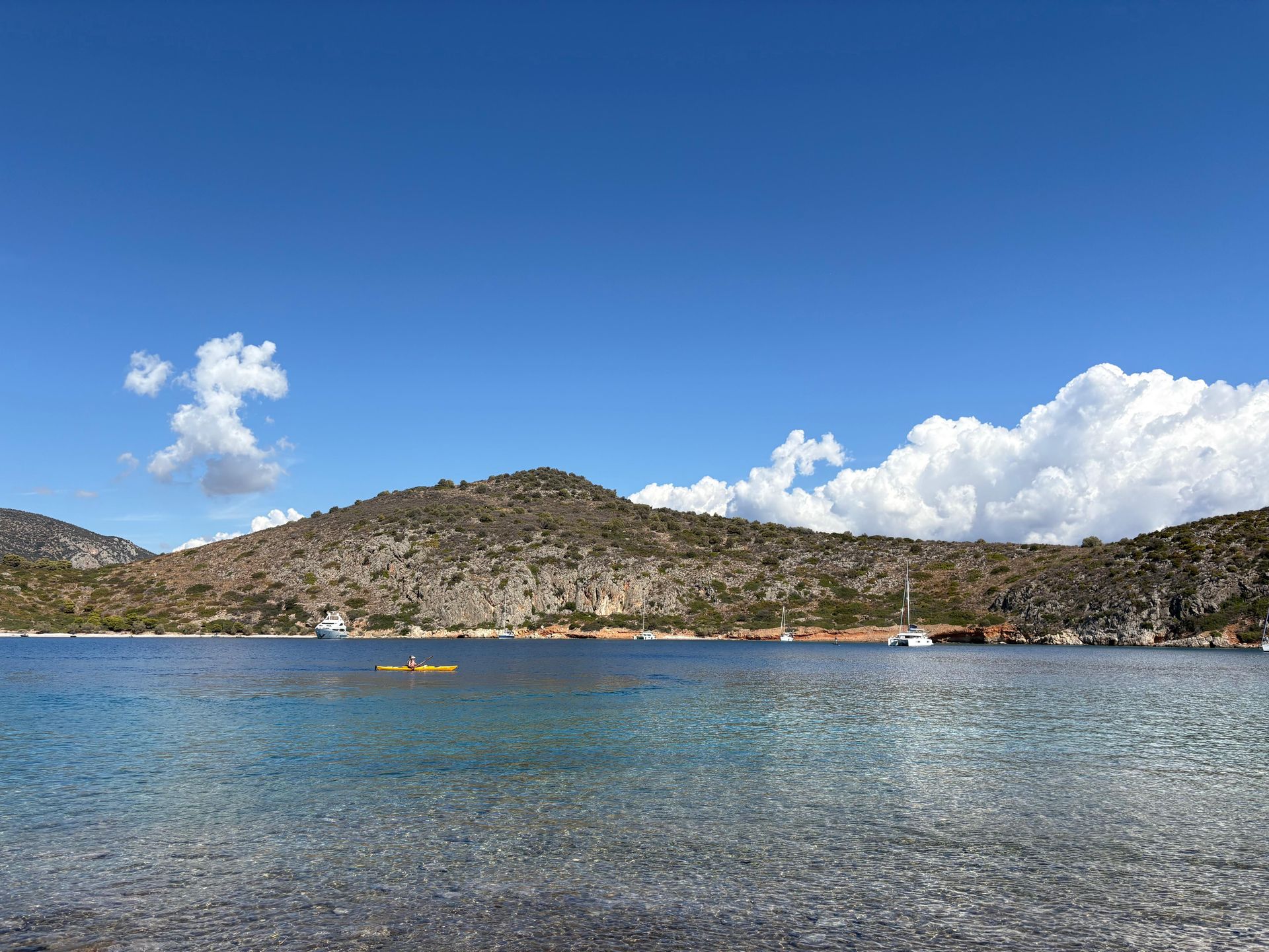 Ruhige blaue Bucht mit felsigen Hügeln, ein kleines gelbes Kajak und weiße Wolken am klaren Himmel