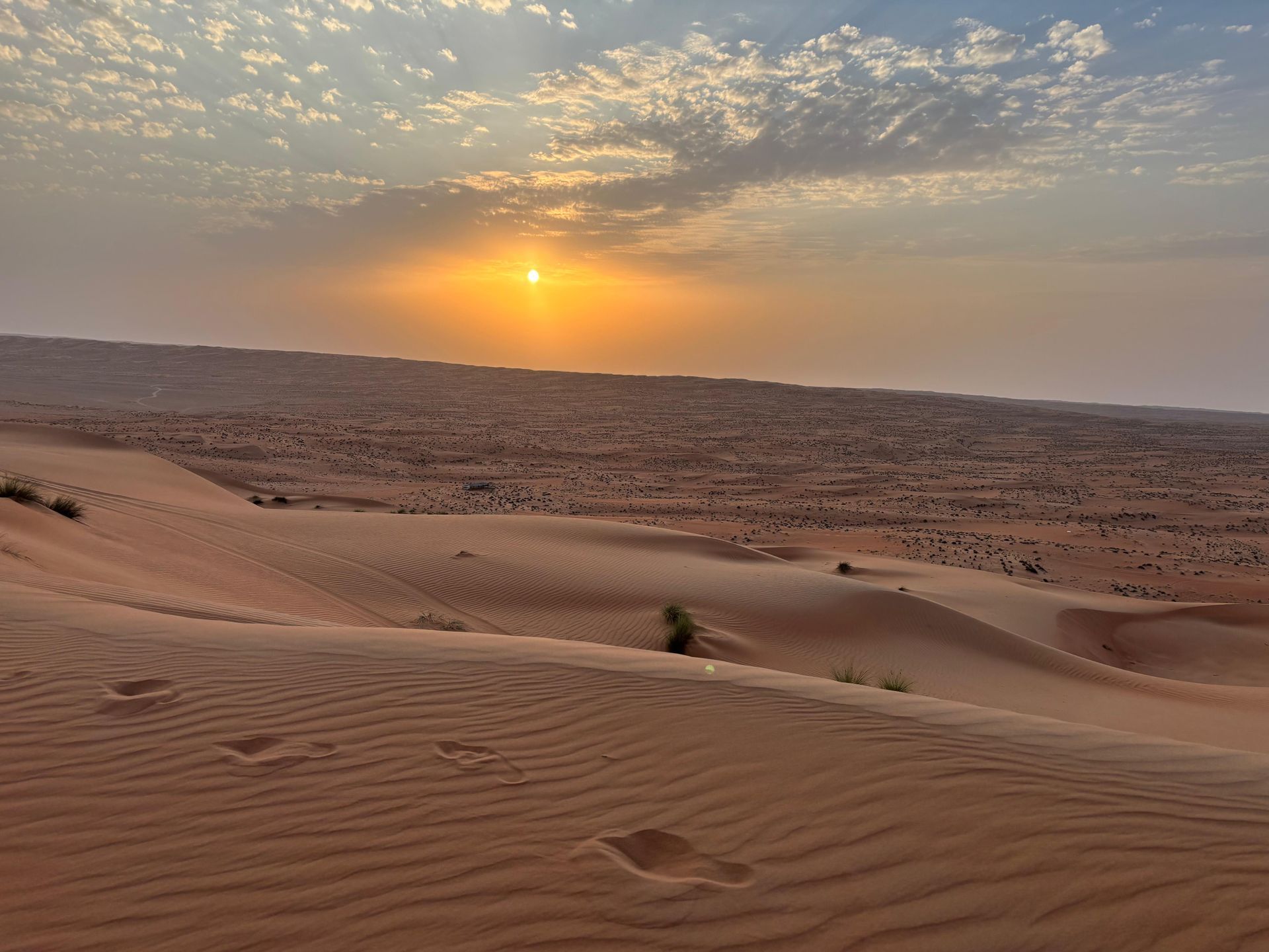 Sonnenuntergang über gewellten Sanddünen unter einem bewölkten Wüstenhimmel