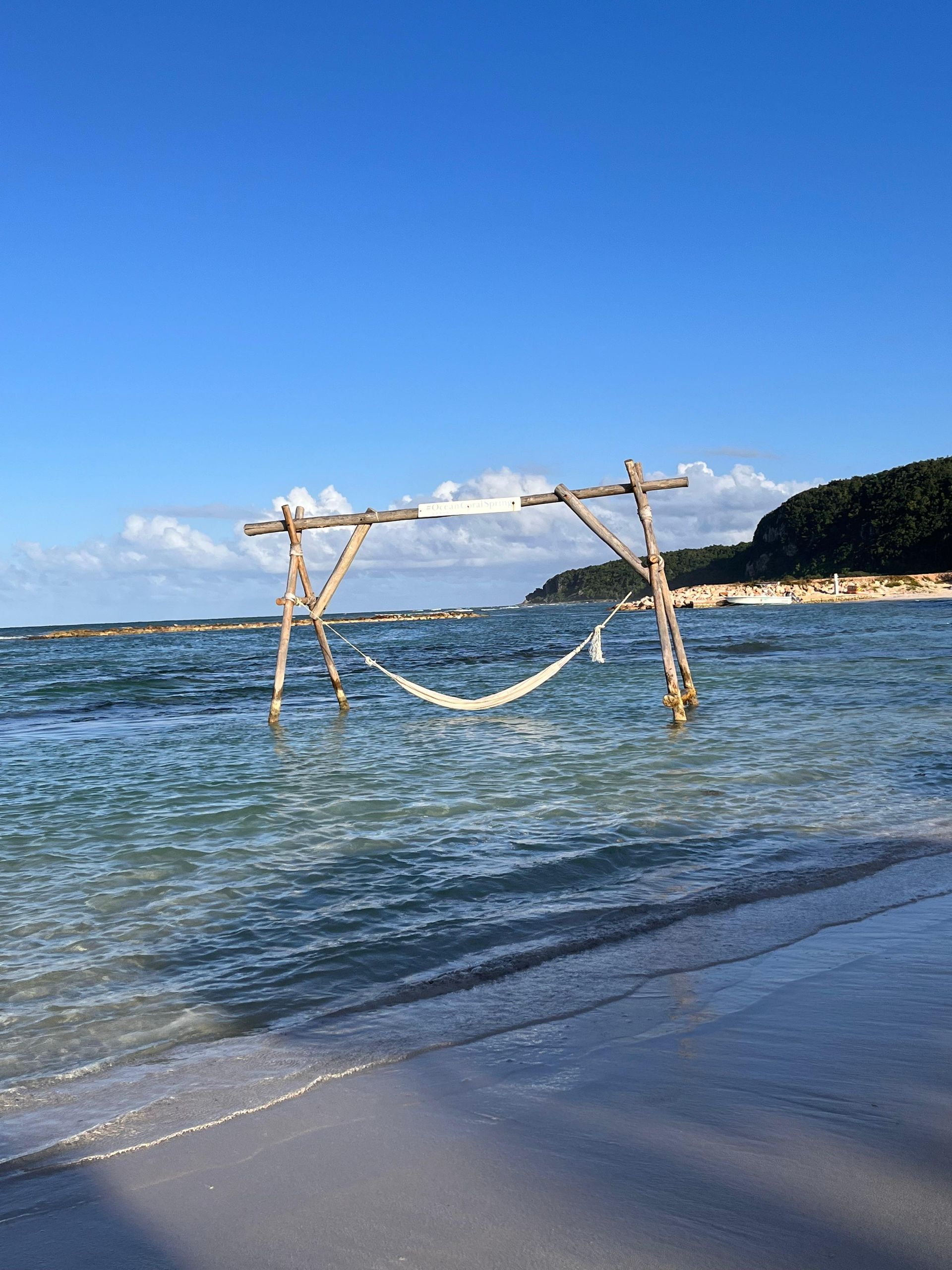 Eine hölzerne Schaukel im flachen Meerwasser unter klarem blauen Himmel, in der Nähe eines Sandstrandes
