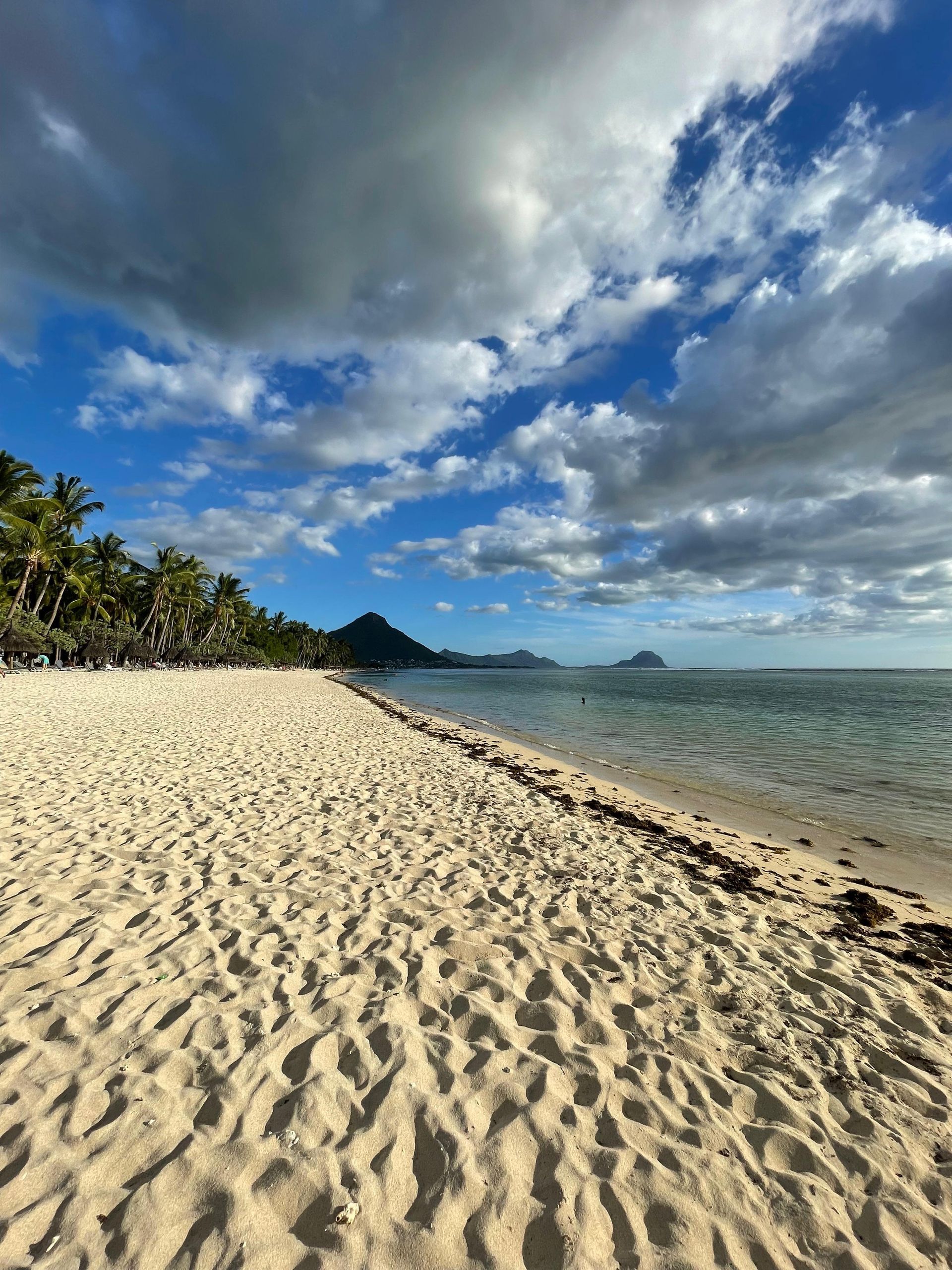 Tropischer Strand mit weißem Sand, türkisfarbenem Wasser, Palmen und Wolkenhimmel