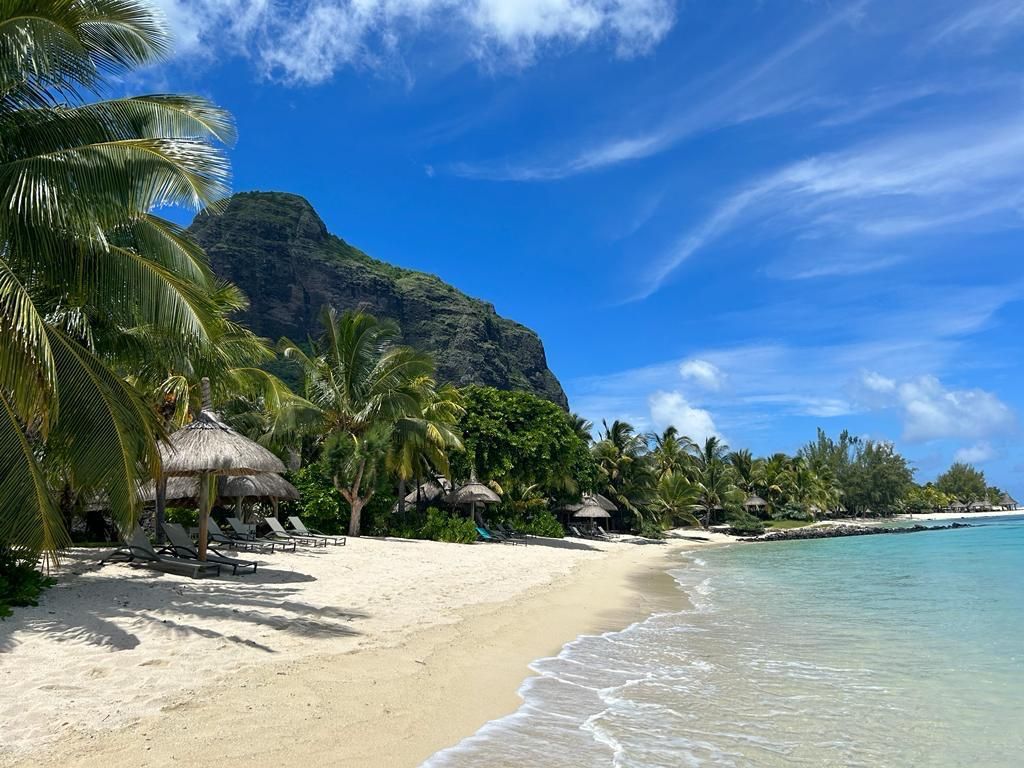 Sonniger Tropenstrand mit Palmen, weißem Sand und klarem blauem Wasser neben einem üppig grünen Berg