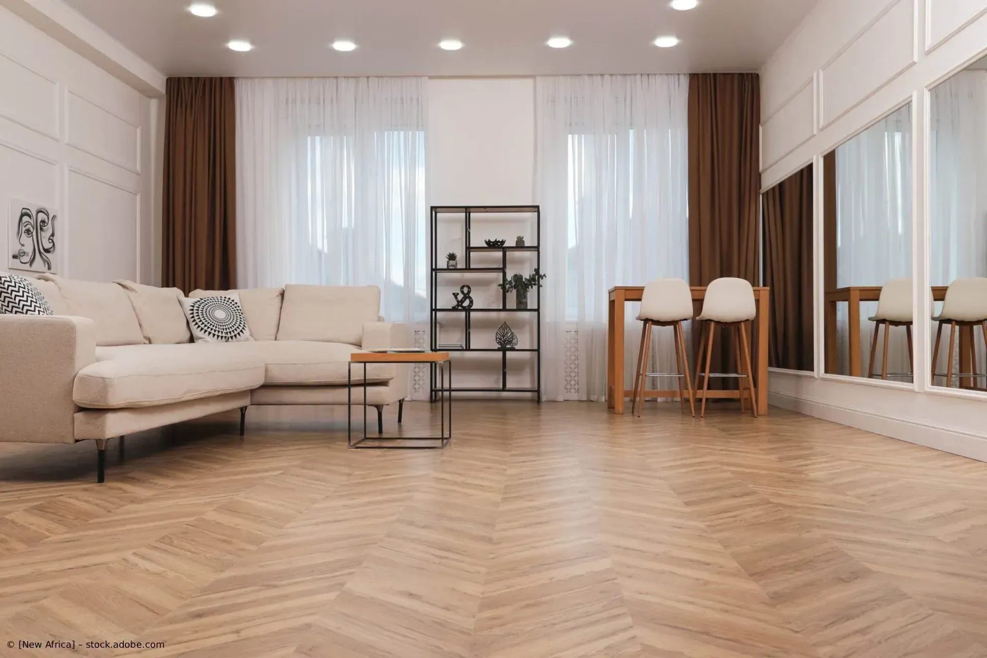 Helles, modernes Wohnzimmer mit beigefarbenem Sofa, Holzboden, Esstisch, Regalen und großen Fenstern