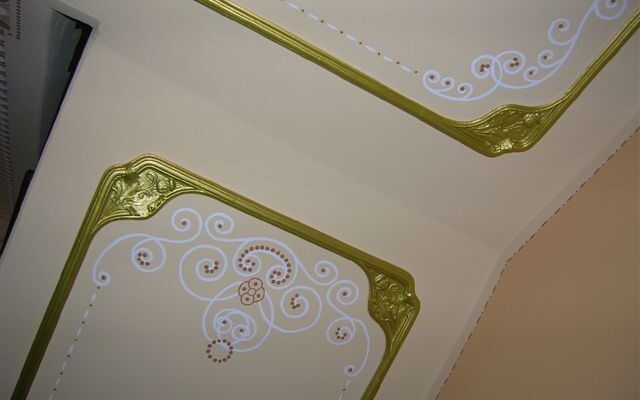 Dekorative Decke mit weiß-goldenen, kunstvollen Ranken in einer Zimmerecke