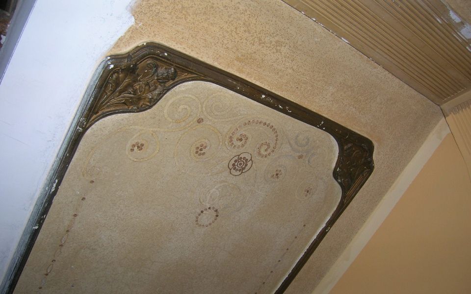 Deckenecke mit Wasserschäden, Schimmelflecken und abblätternder Farbe um eine Lüftungsöffnung