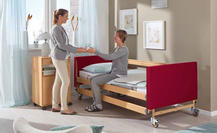 Eine Frau steht neben einer Frau, die in einem Krankenhausbett sitzt.