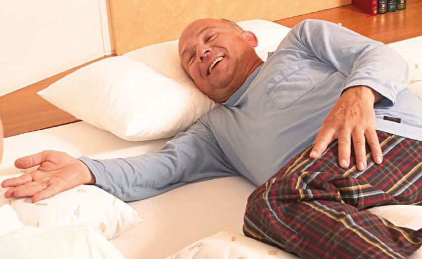 Ein Mann liegt auf einem Bett mit einem Kissen, auf dem „a“ steht