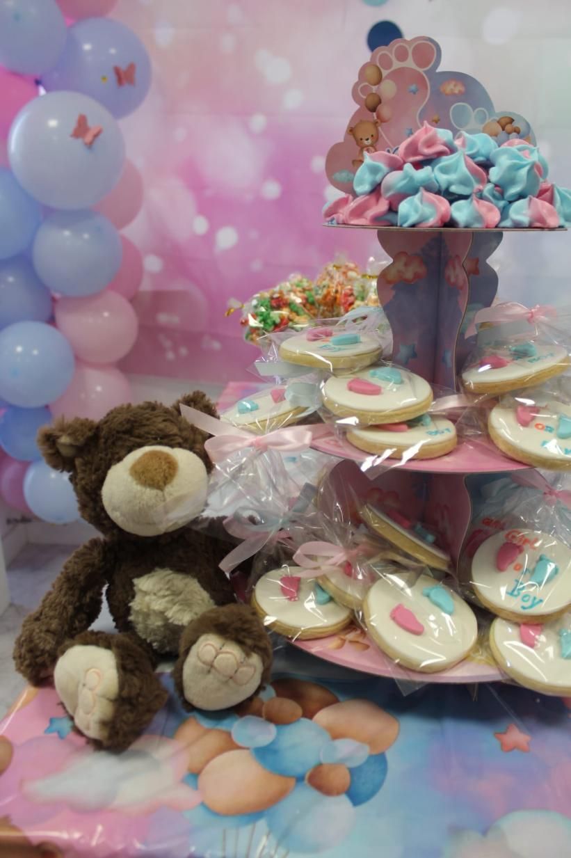 Osito de peluche y golosinas en un baby shower con globos y un puesto de postres escalonado.