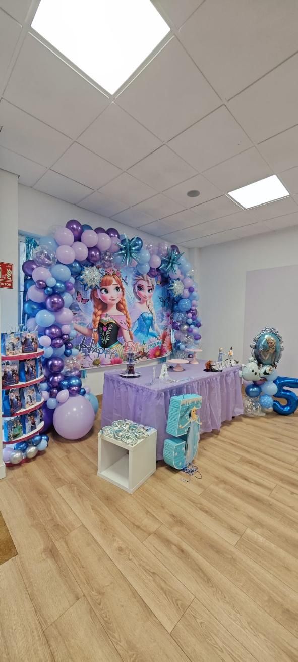 Decoraciones de fiesta con temática de Frozen en una habitación, que incluyen una mesa, globos y recortes de personajes.
