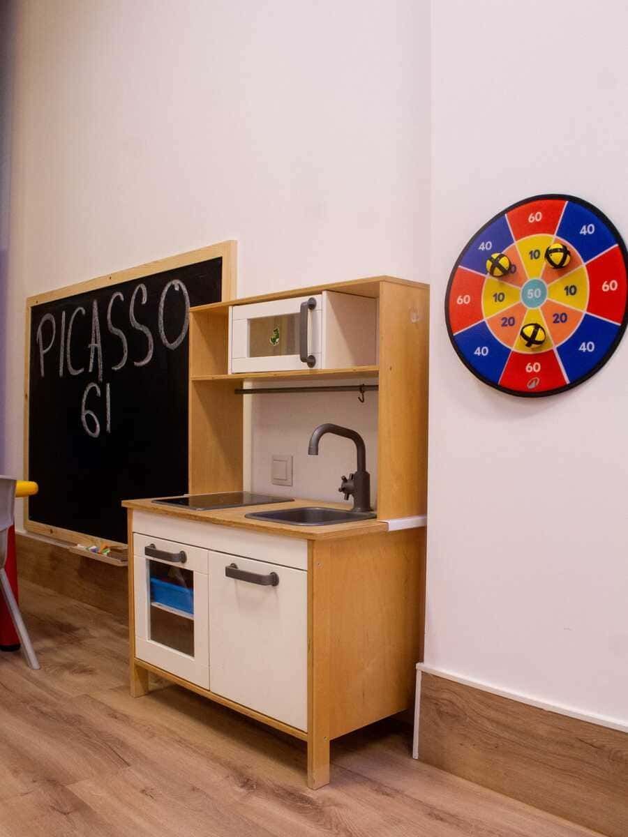 Una cocinita de juguete en el aula, junto a una pizarra con la inscripción 