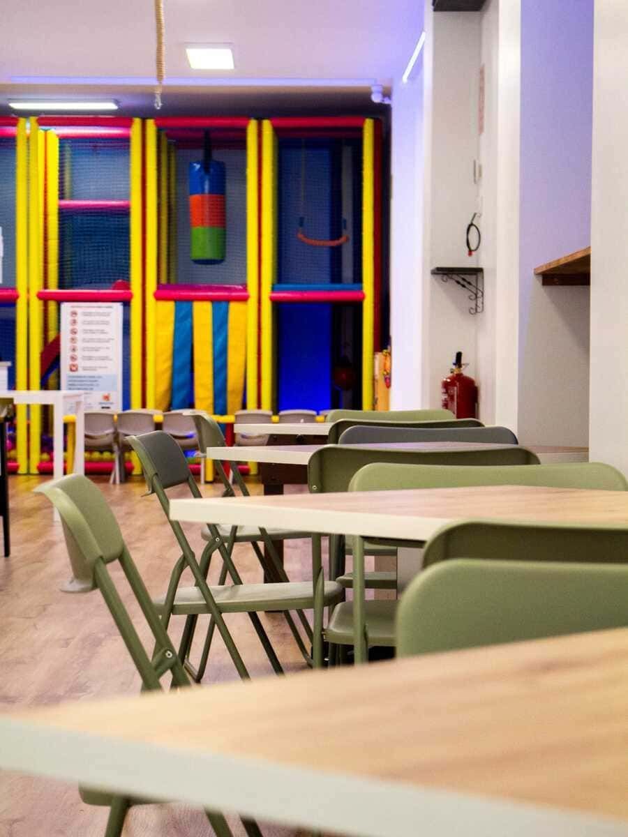 Zona de juegos interior colorida con mesas y sillas verdes en primer plano.