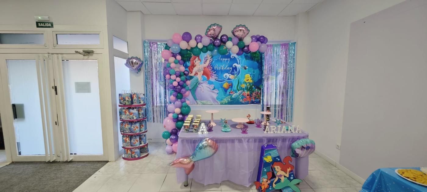Decoración de fiesta con La Sirenita de Disney. Globos, mesa con dulces y fondo con los personajes.
