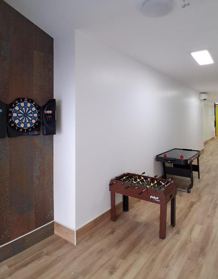 Pasillo con diana de dardos montada en la pared y dos mesas de juego sobre un suelo de madera clara.