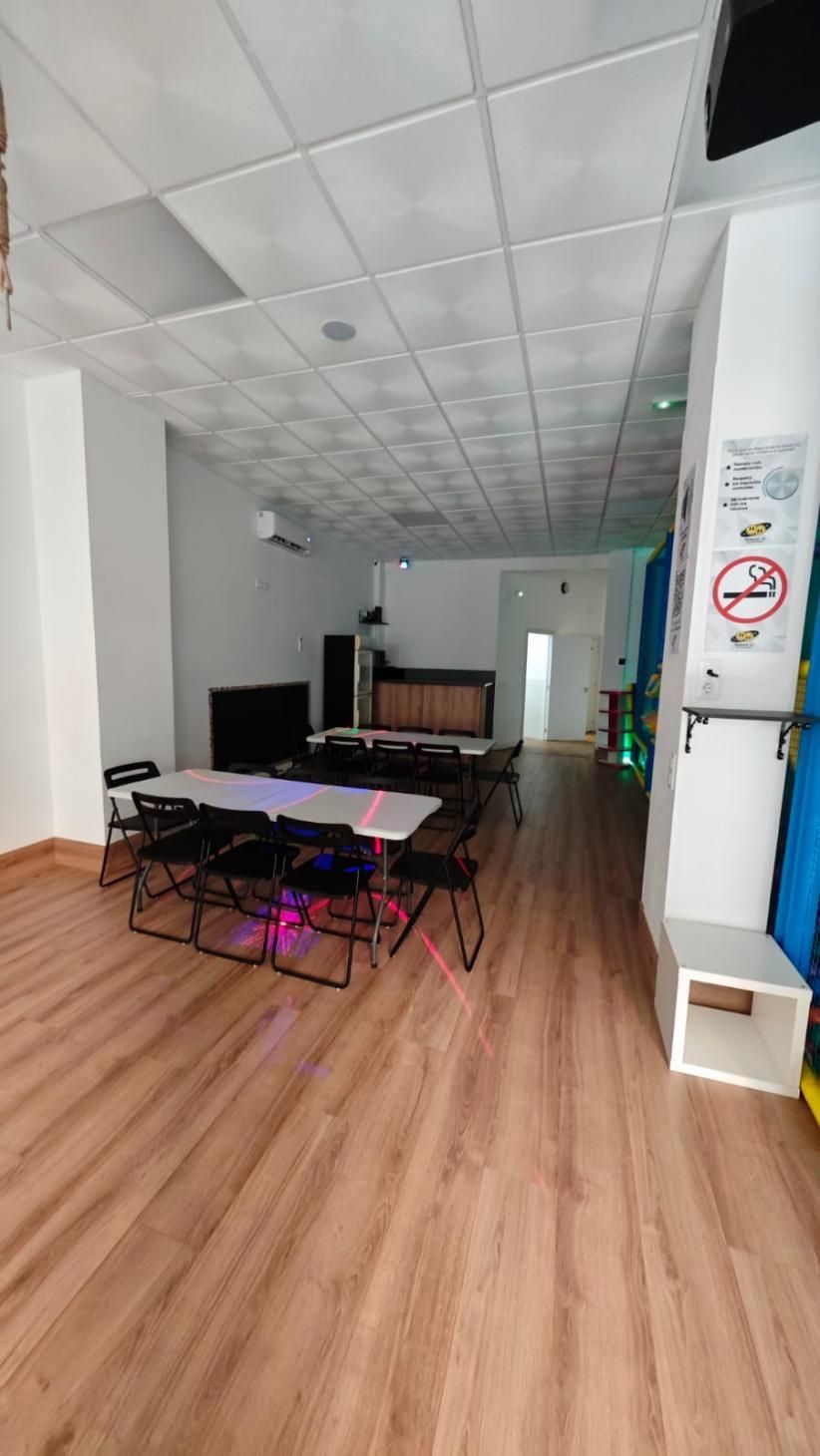 Interior vacío, probablemente un salón de juegos, con mesas, sillas y una zona de bar.