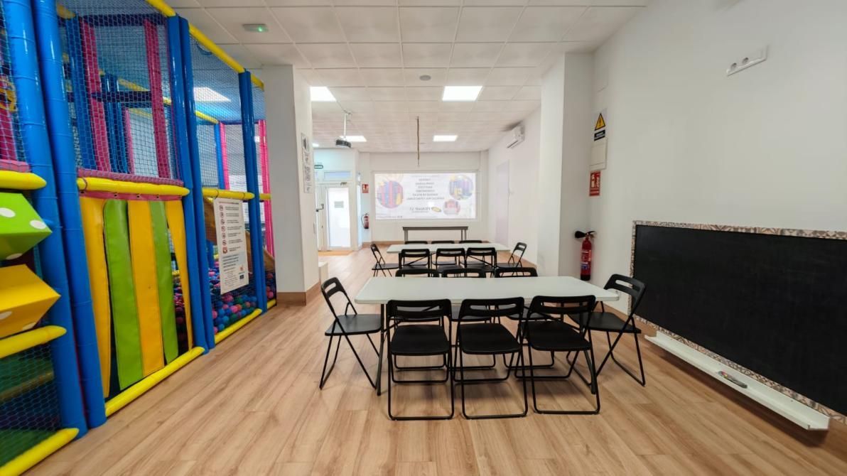 Área de juegos interior con una colorida estructura de escalada, mesas y sillas.