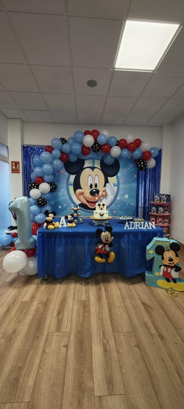 Decoraciones para fiesta de cumpleaños con temática de Mickey Mouse. Globos, pastel y fondo con el personaje.
