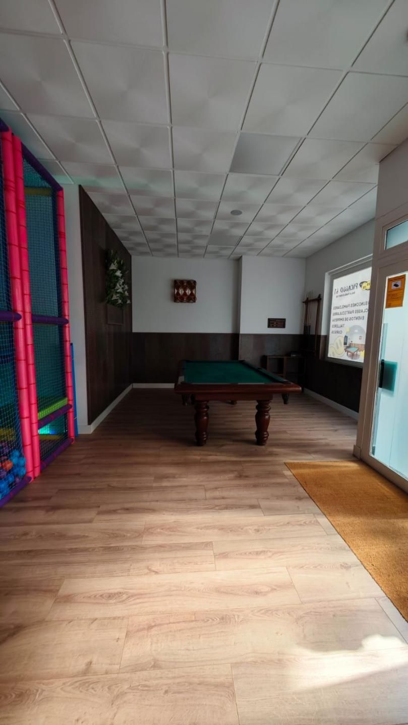 Mesa de billar en una habitación con piscina de pelotas, paneles oscuros, piso de madera clara y una puerta.