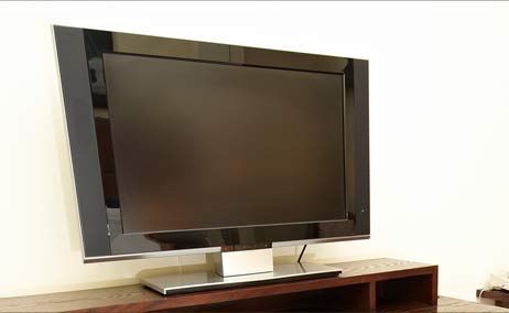 Televisor de pantalla plana grande de color negro sobre un soporte de madera contra una pared de color claro.
