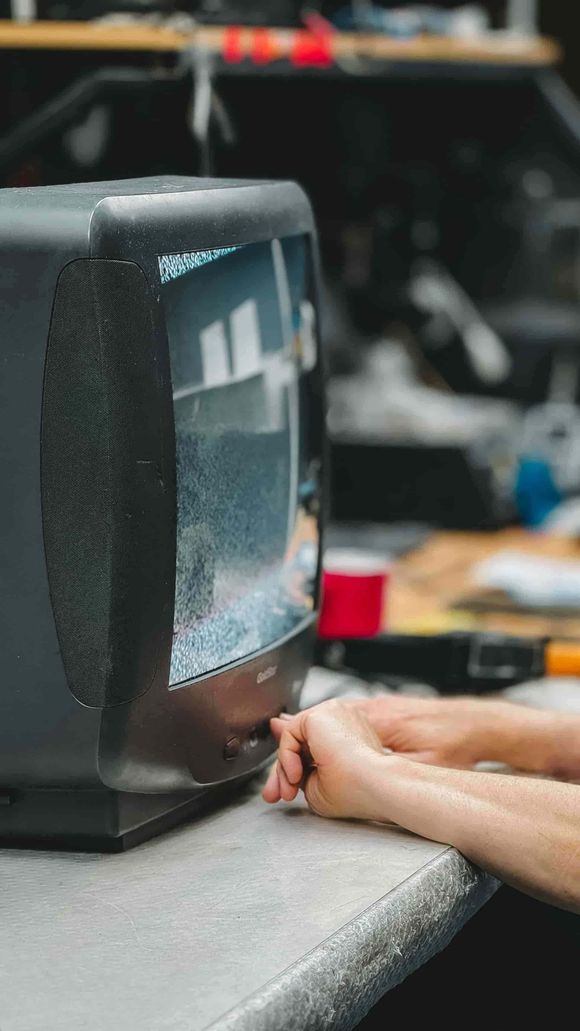 Televisor CRT negro que muestra estática, con manos apoyadas sobre una mesa.