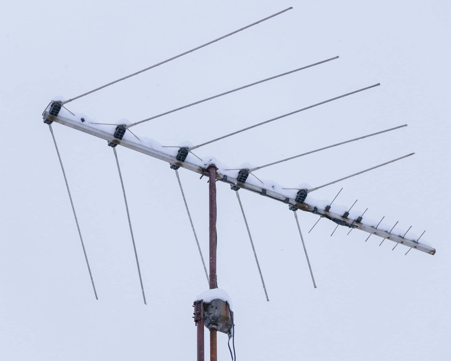 Antena de televisión cubierta de nieve contra un cielo nublado.