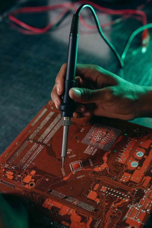 Soldadura manual de componentes electrónicos en una placa de circuito roja con un soldador.