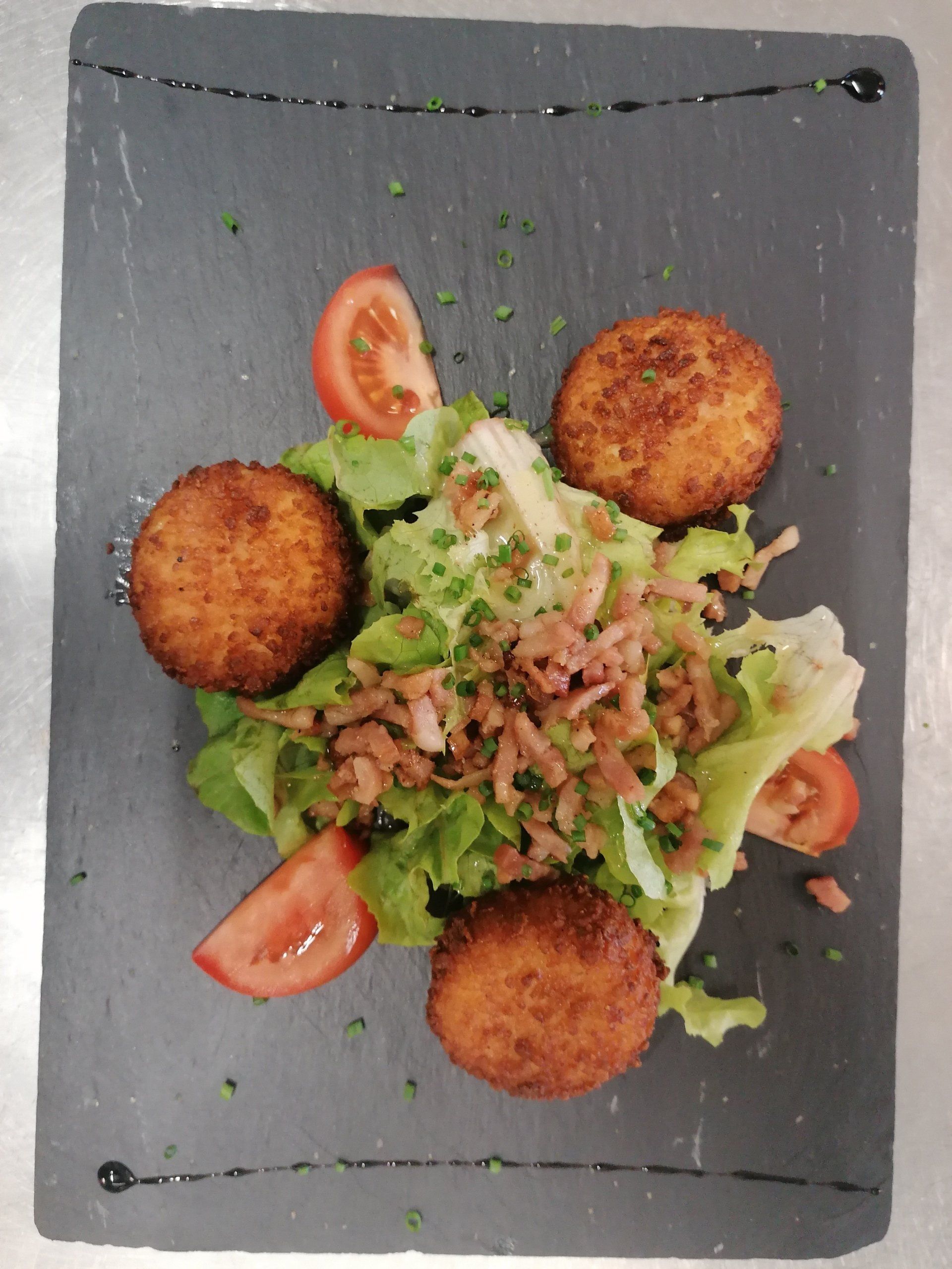 Une salade avec des lardons, des tomates et du fromage pané