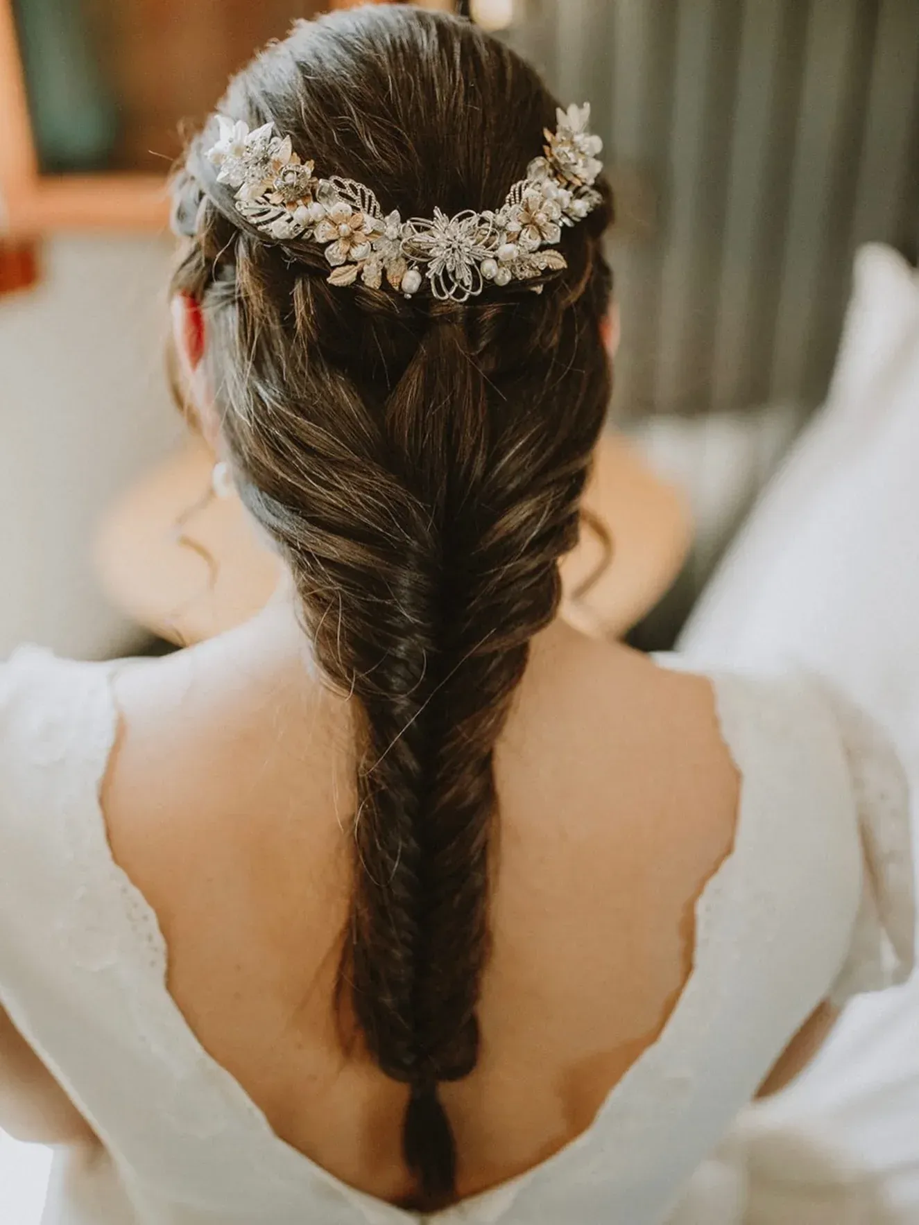 Mujer de cabello castaño con un peinado de cola de pez trenzada, con un tocado floral y un vestido blanco.