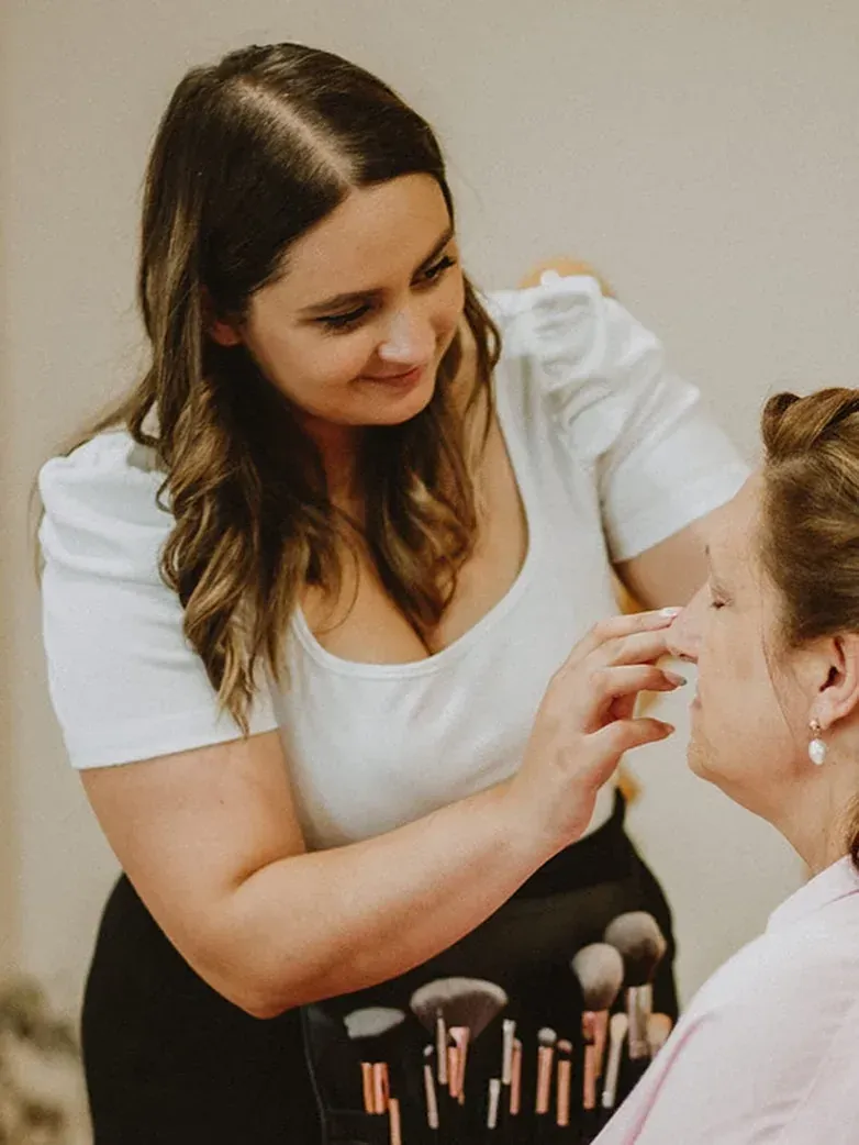 Artista de maquillaje aplicando maquillaje en el rostro de un cliente, en un entorno interior.